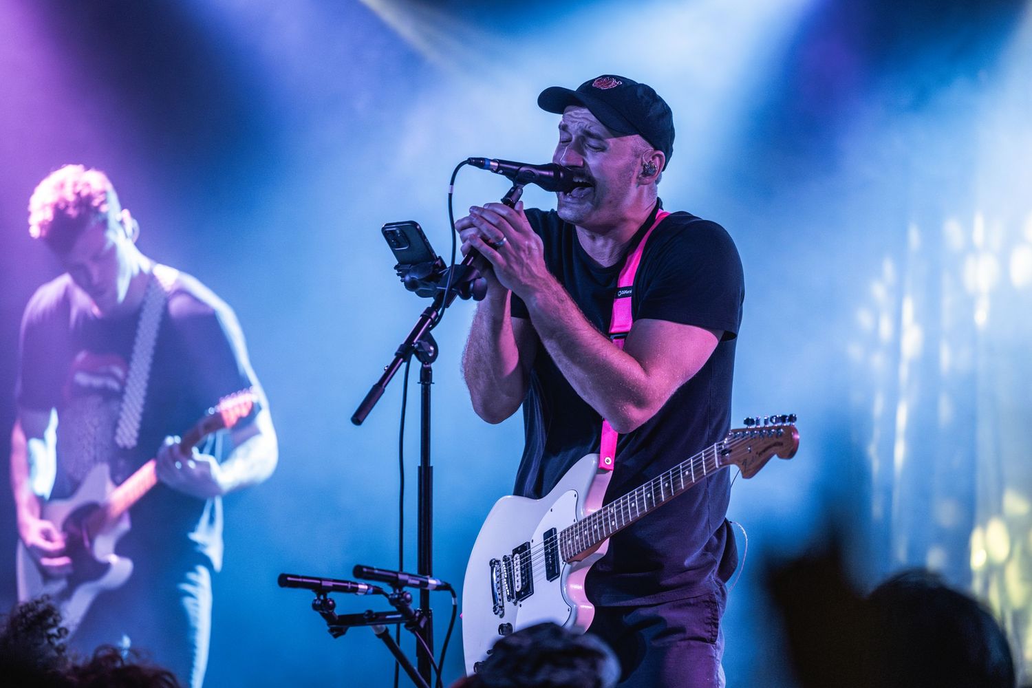 Musician plays guitar and sings into microphone with blue stage lights creating dramatic atmosphere.