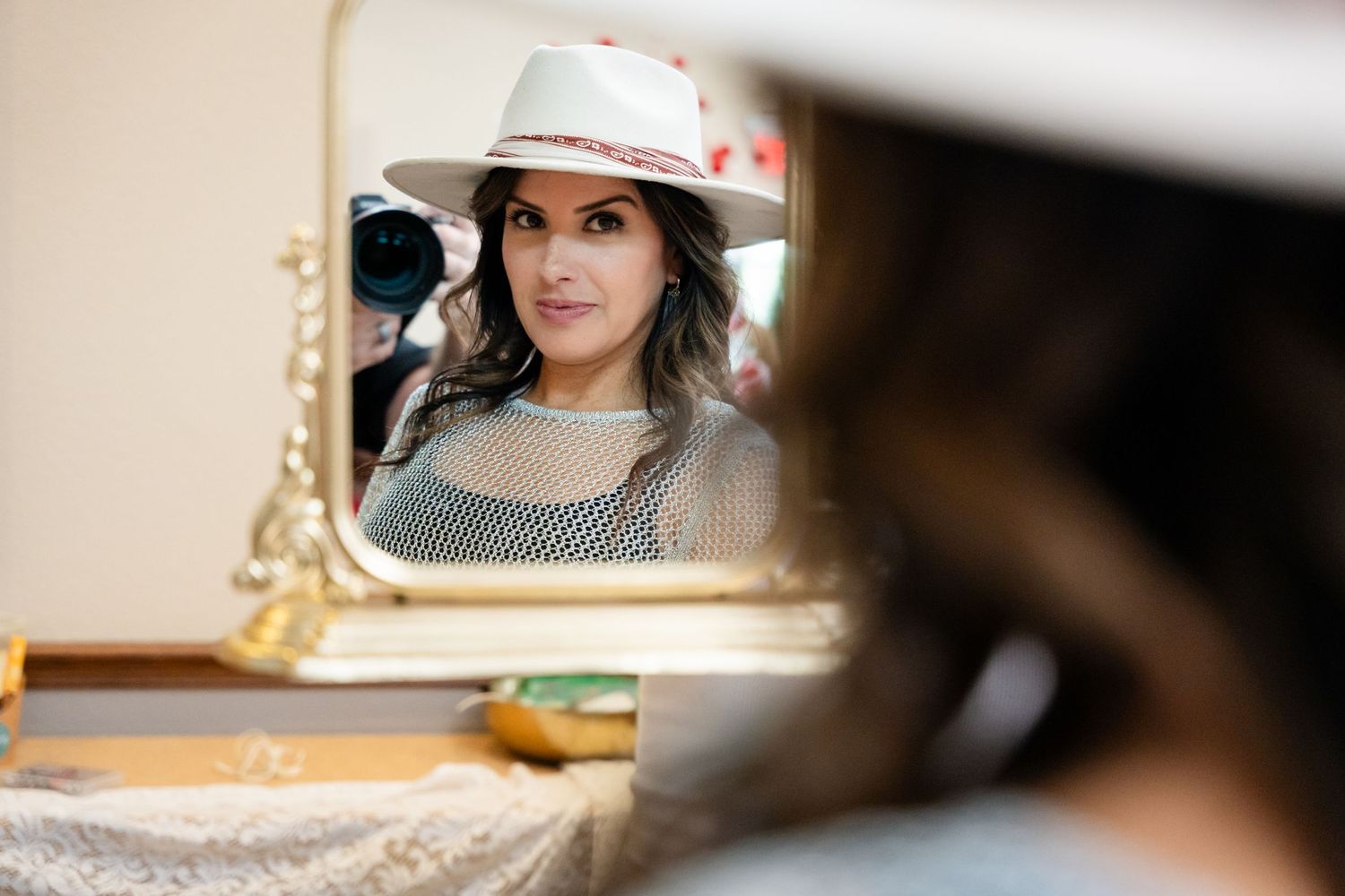 Reflection in ornate gold mirror showing someone wearing a patterned hat.