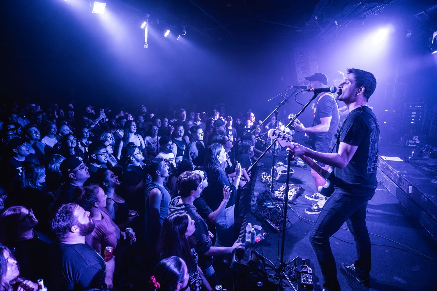 A performer sings into a microphone on stage while an energetic crowd watches during a concert with blue lighting effects.