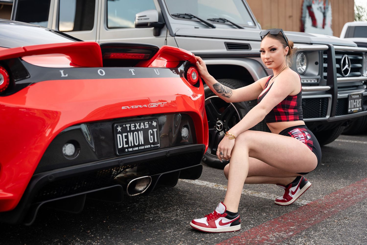 Model in athletic wear poses next to red sports car showing off rear bumper details.