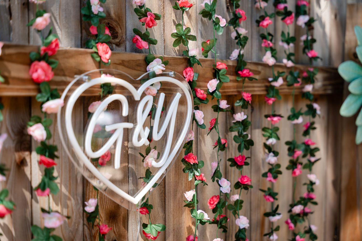 Decorative heart-shaped 'G&Y' sign surrounded by pink roses and greenery on wooden backdrop.