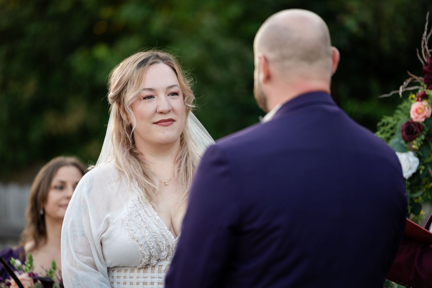A couple exchanges vows under a floral arch during an outdoor wedding ceremony.