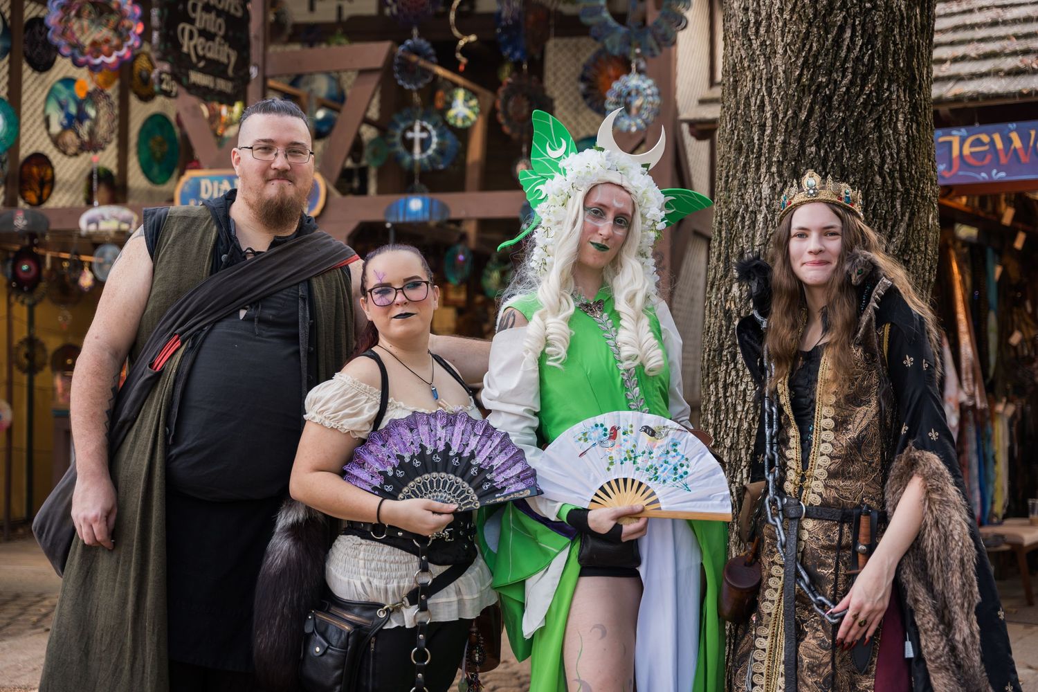 Group in fantasy costumes poses at renaissance faire in medieval marketplace setting.