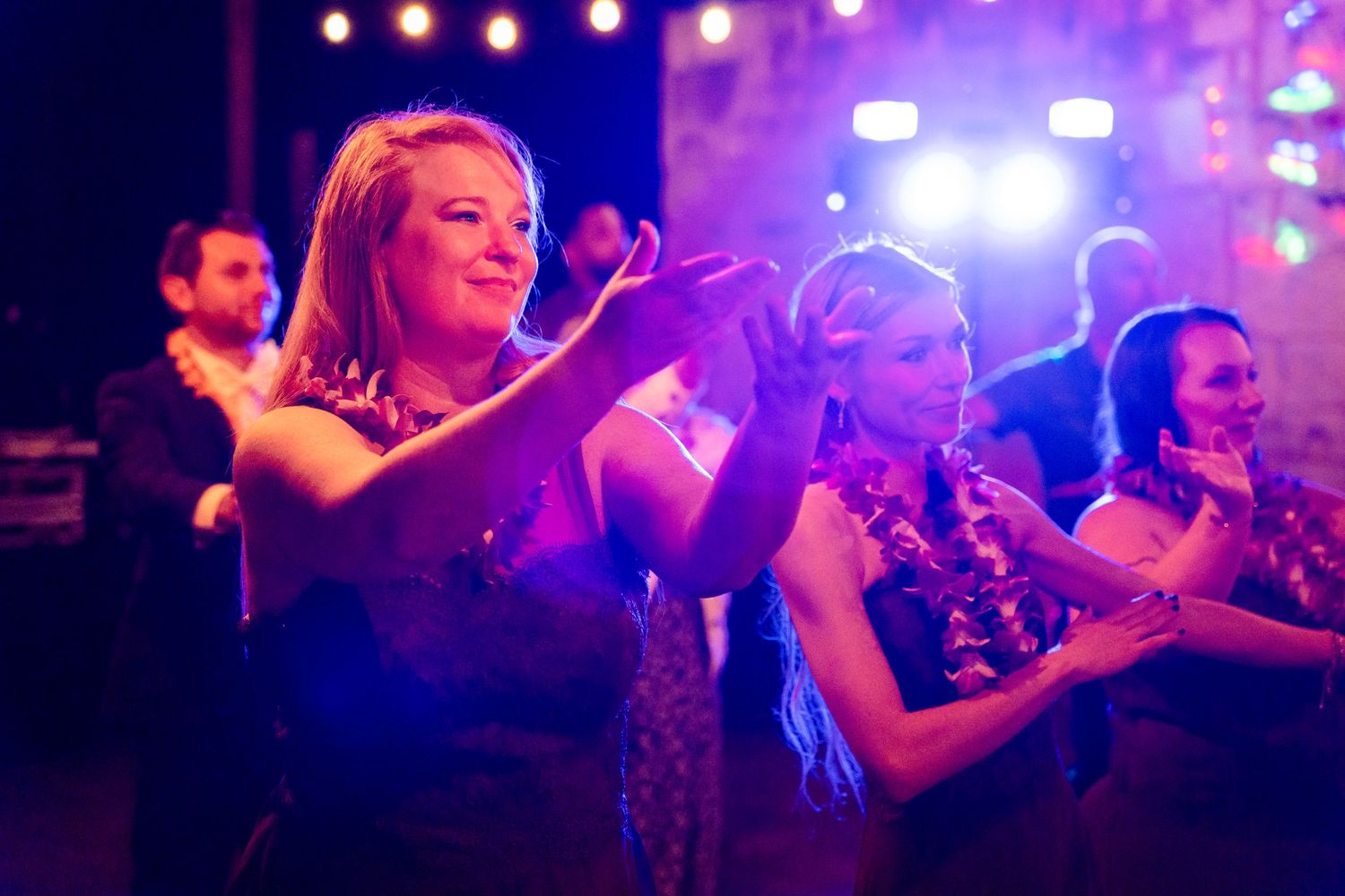 Wedding guests dancing and celebrating under colorful party lights.