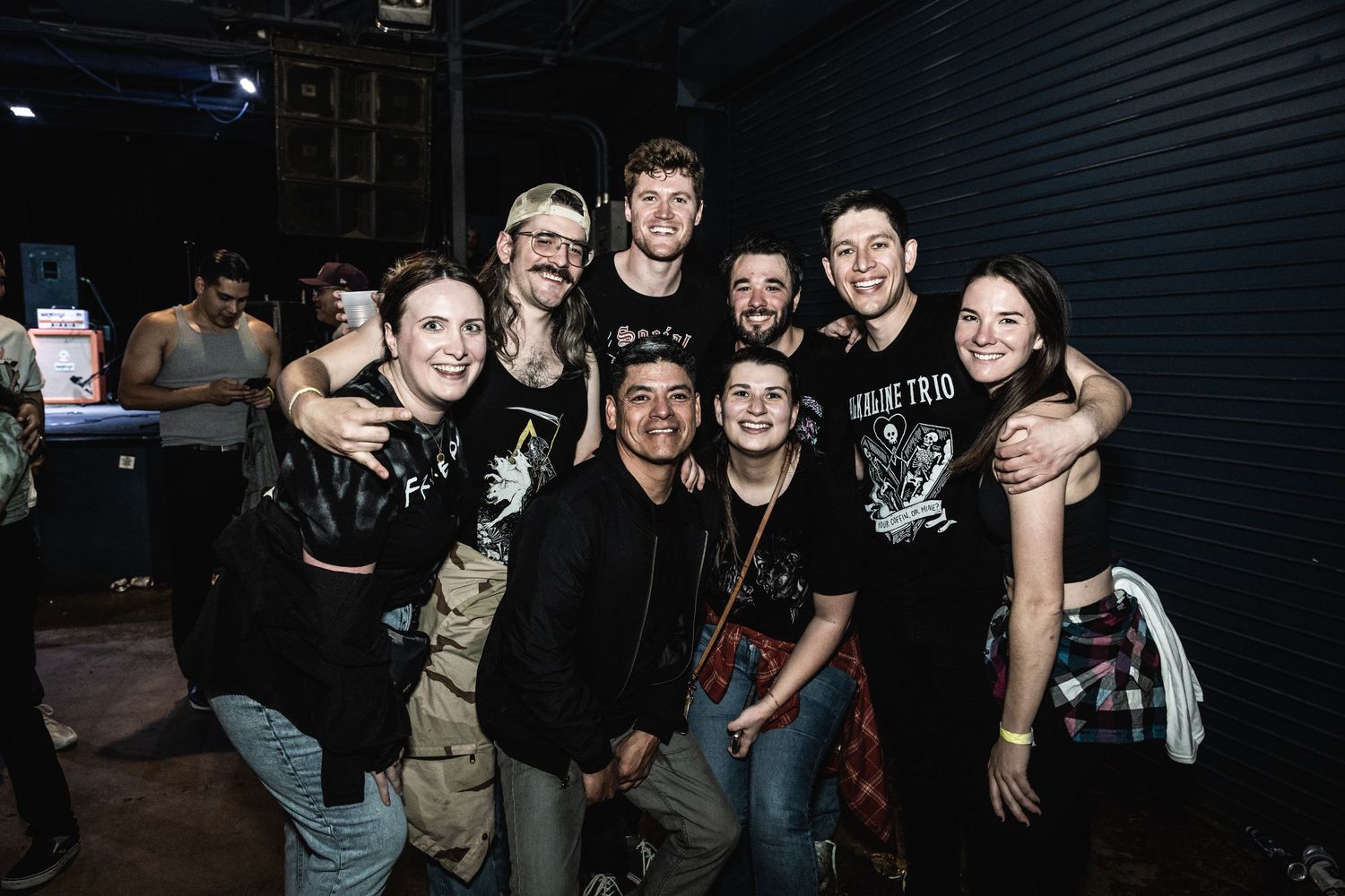 Group photo of band members and fans posing together backstage after a concert.