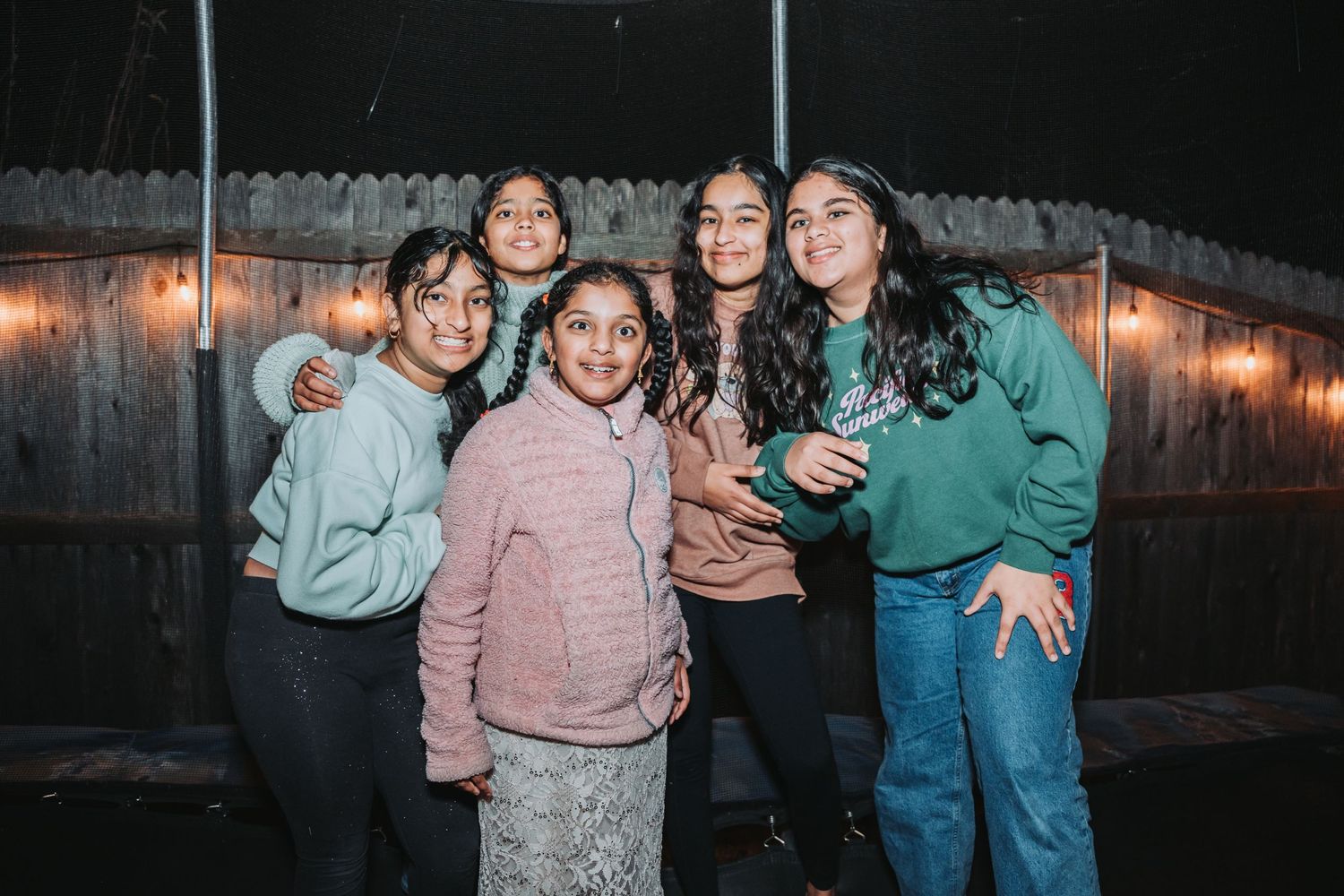 Group photo of friends in casual attire standing together against wooden fence at night.
