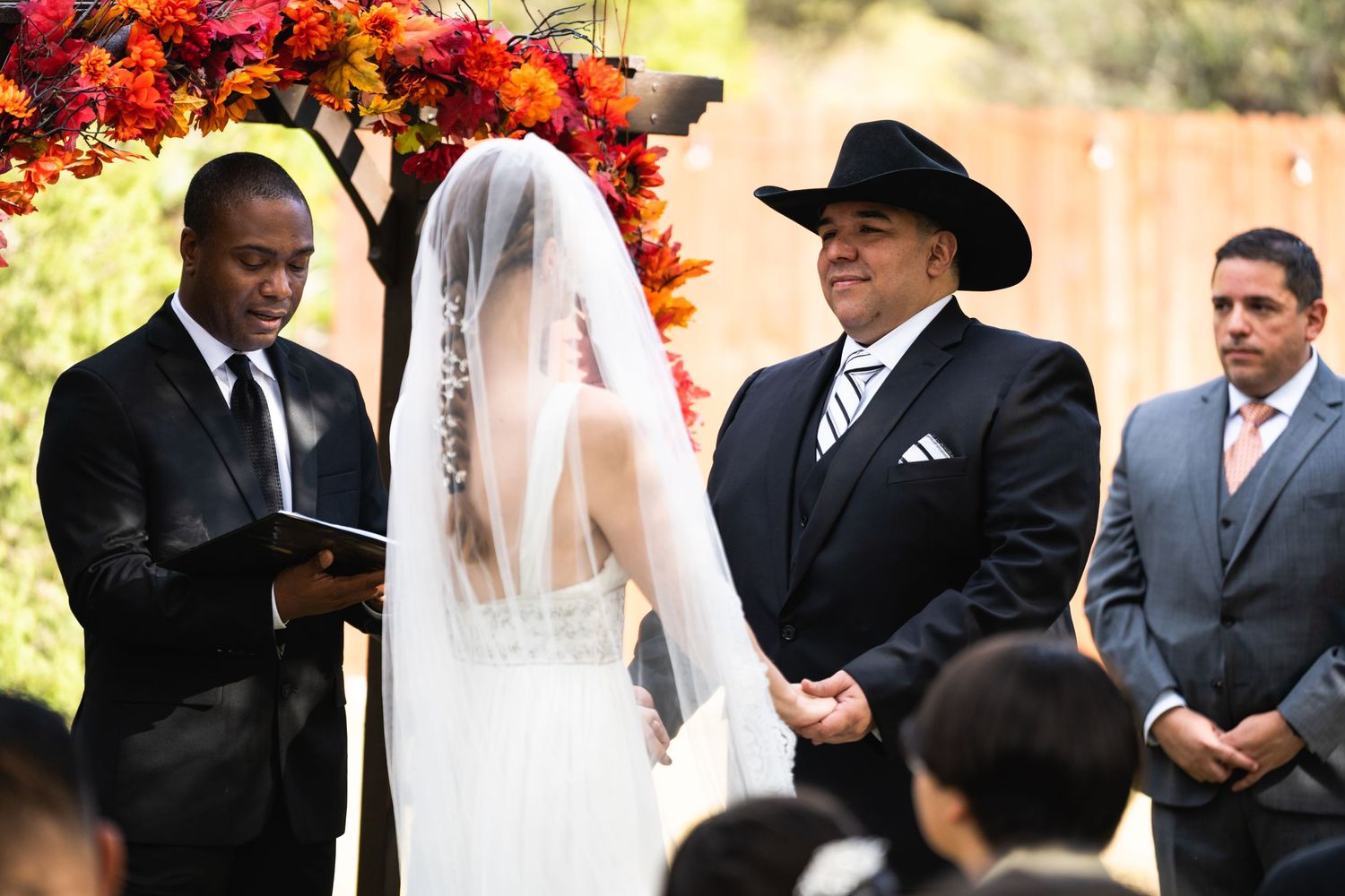 Wedding ceremony under floral arch with orange and red flowers.