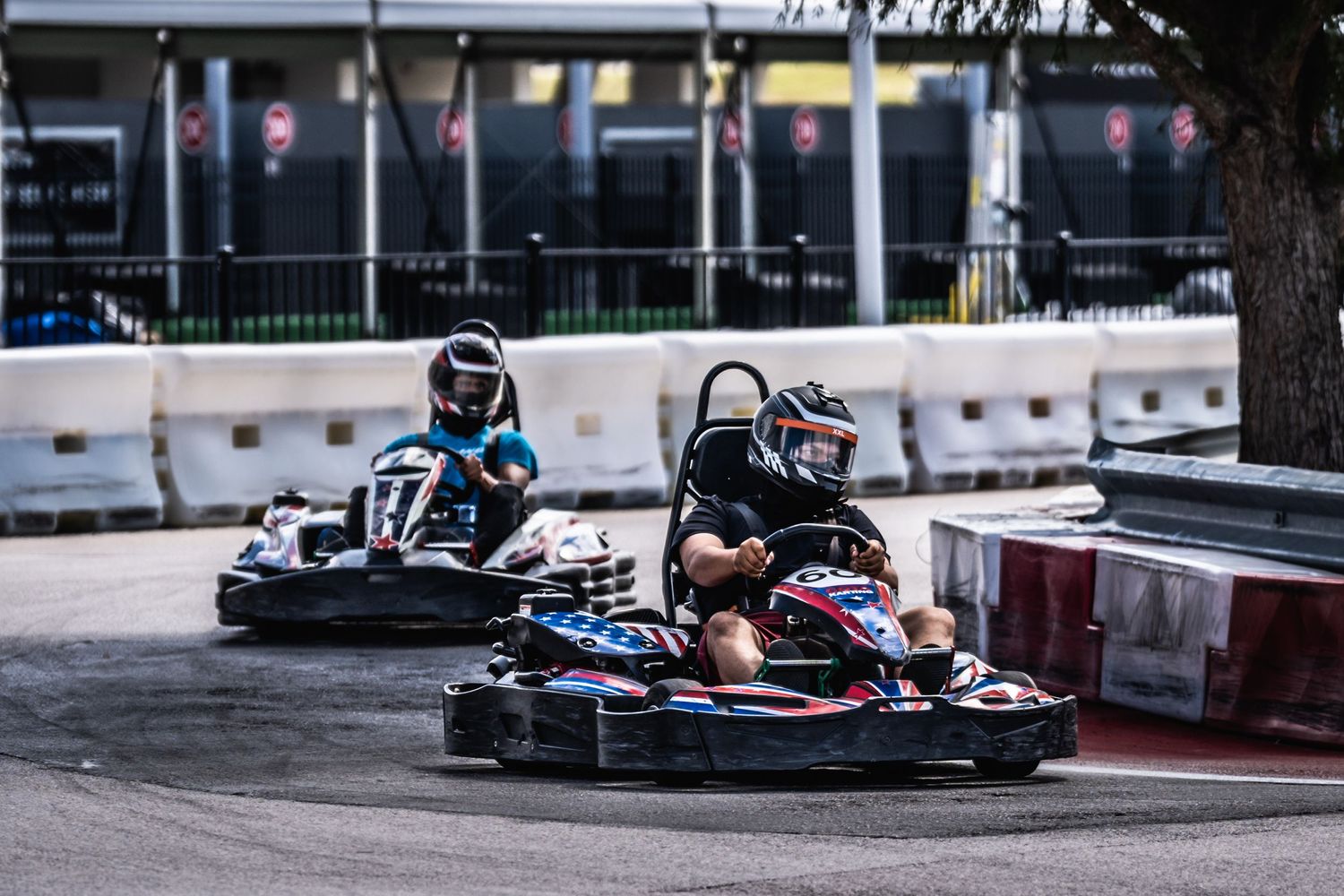 Two go-karts racing neck and neck on indoor karting track.