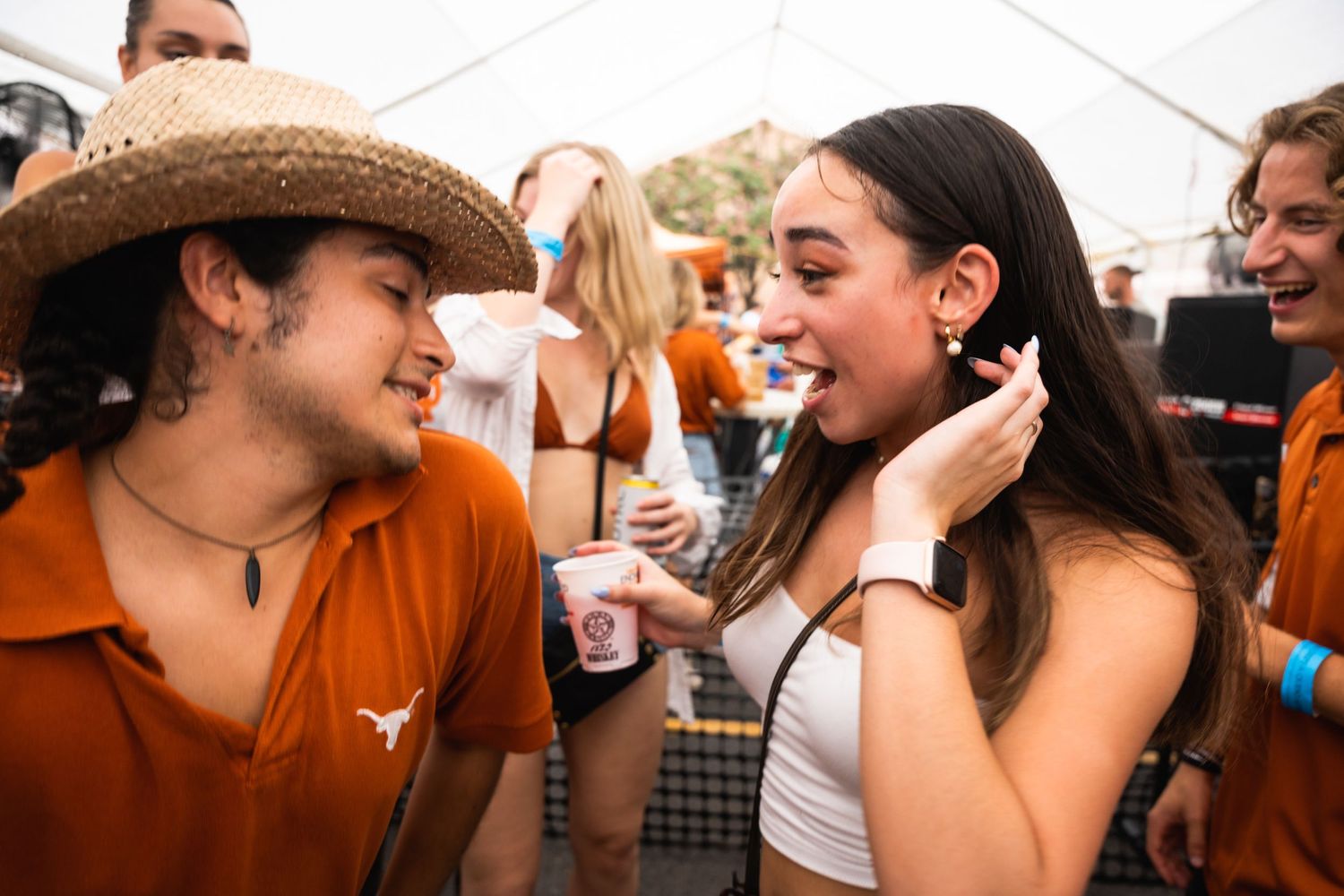 People socializing and laughing at outdoor party under white tent.