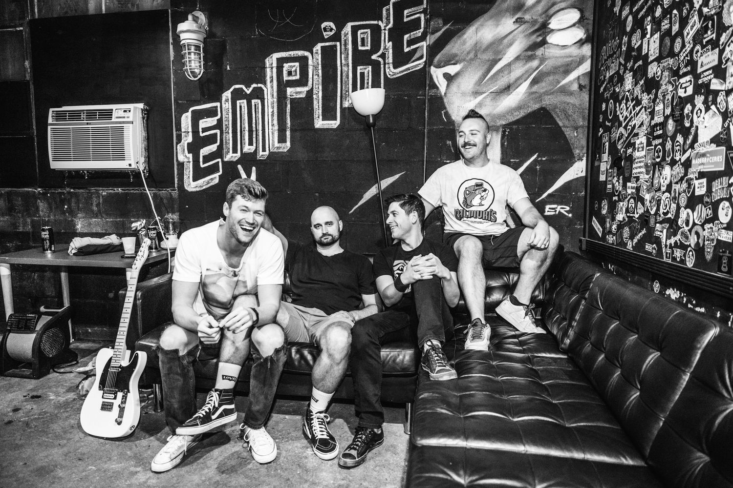 Black and white portrait of band members sitting on couch against graffiti wall.