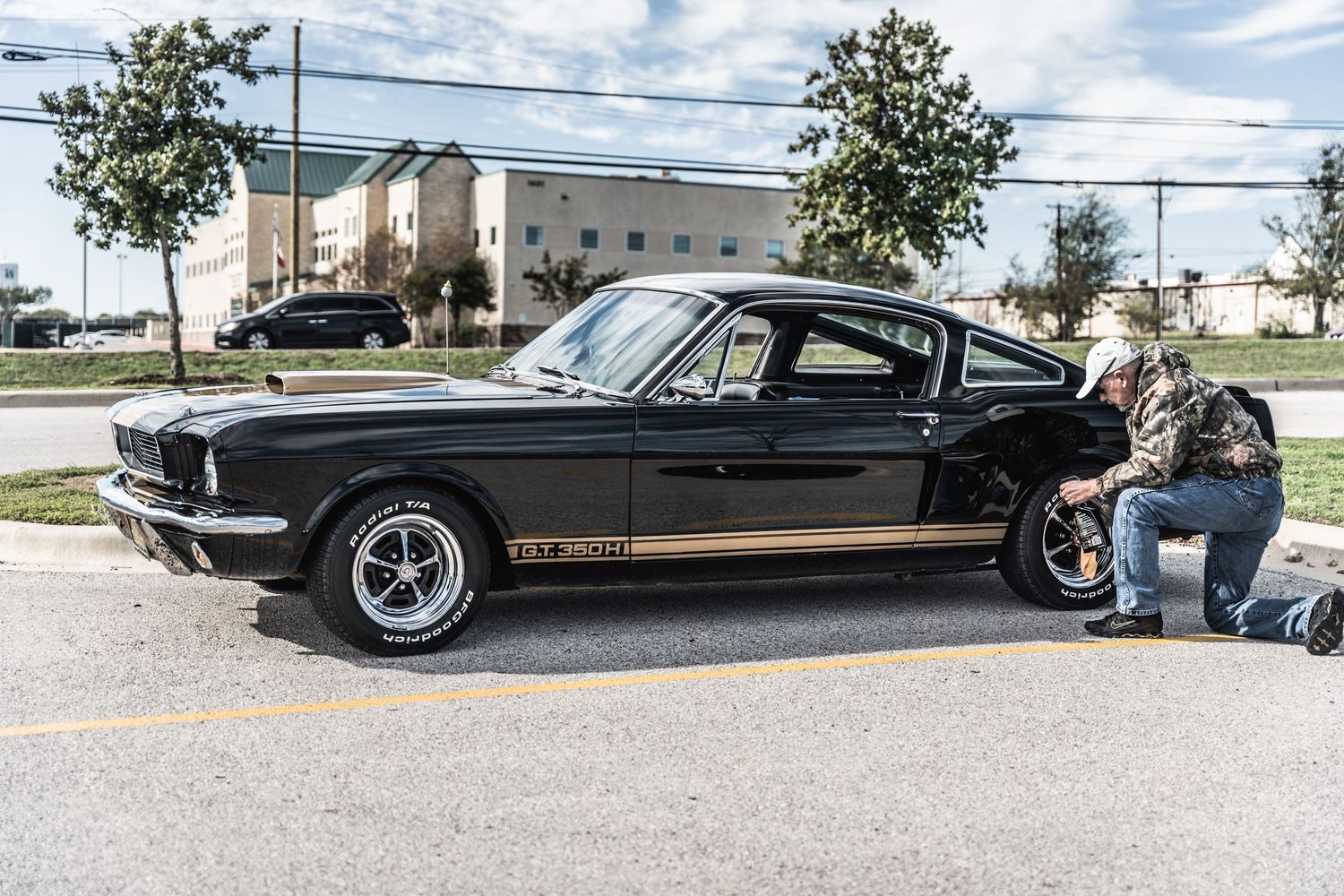 Classic black Ford Mustang Fastback being inspected at outdoor car show.