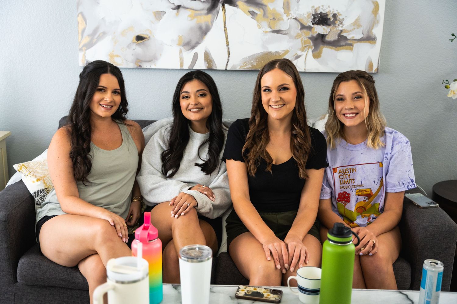 Four women sitting together on a couch smiling during a casual gathering.