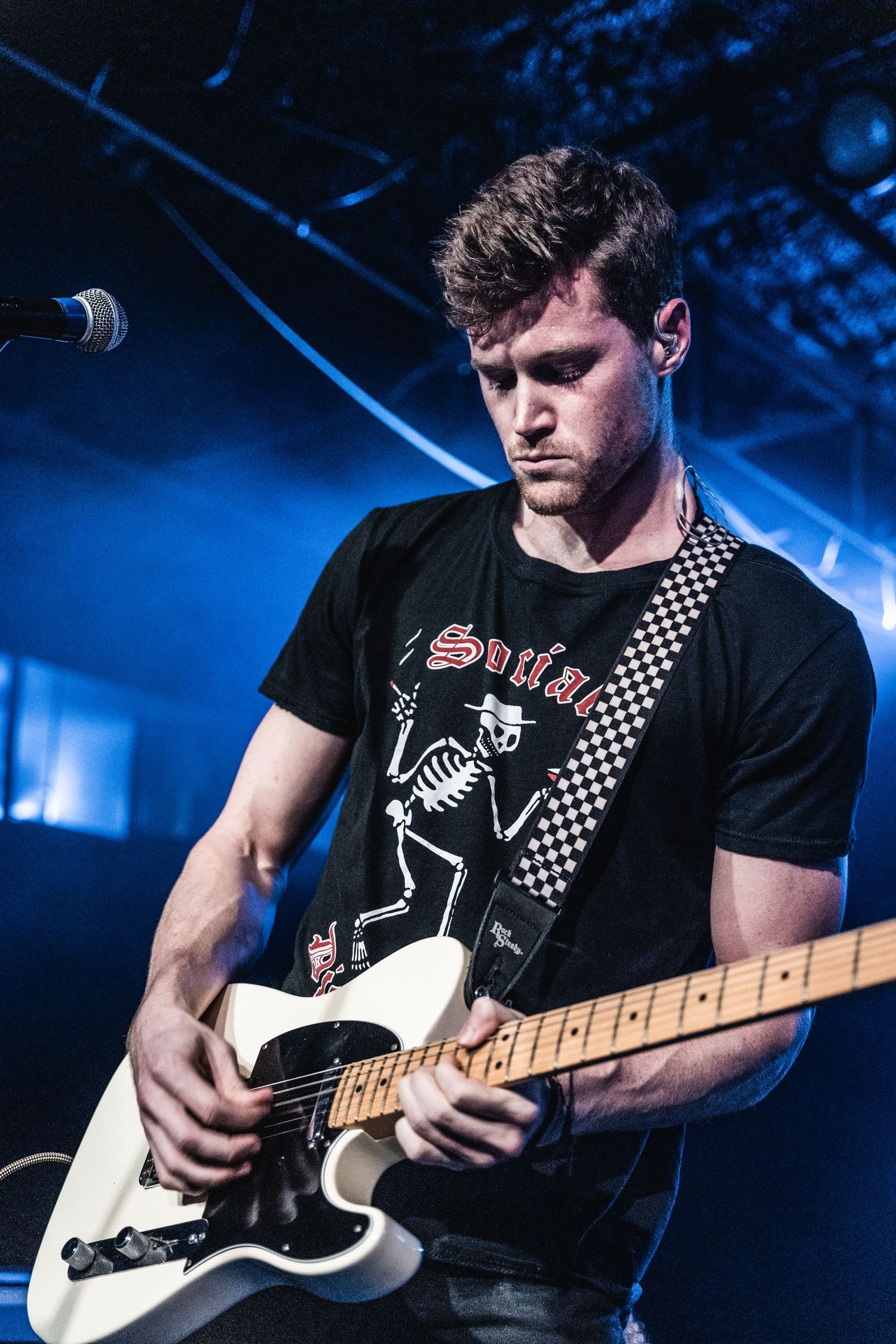 Guitarist performs with white electric guitar under blue stage lighting.