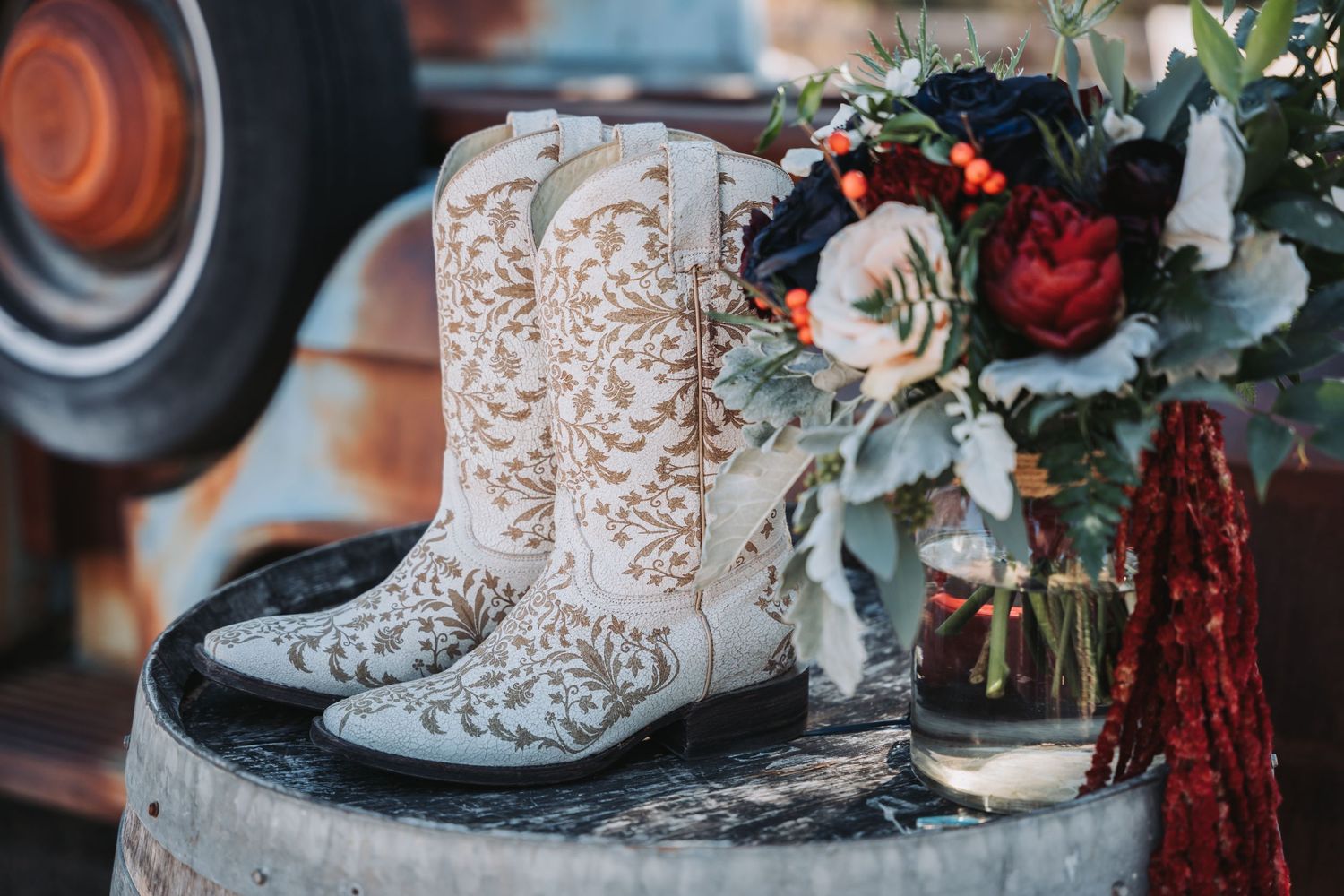 White embroidered cowboy boots next to a burgundy and blush floral bouquet.