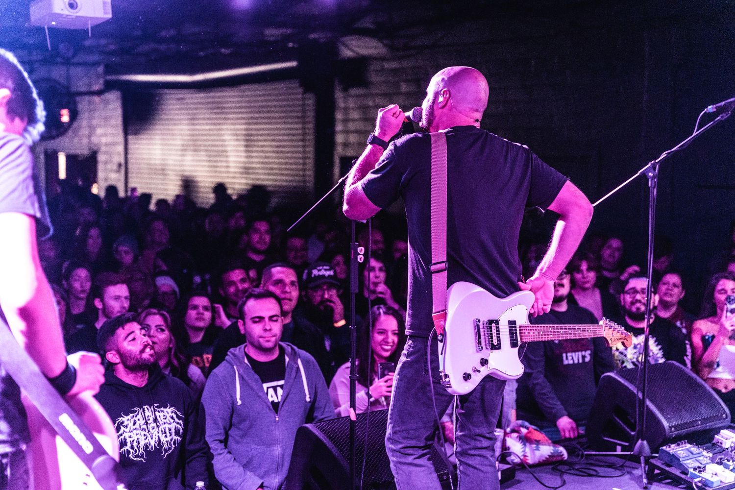 Musicians perform on stage with dramatic lighting while crowd watches intently.