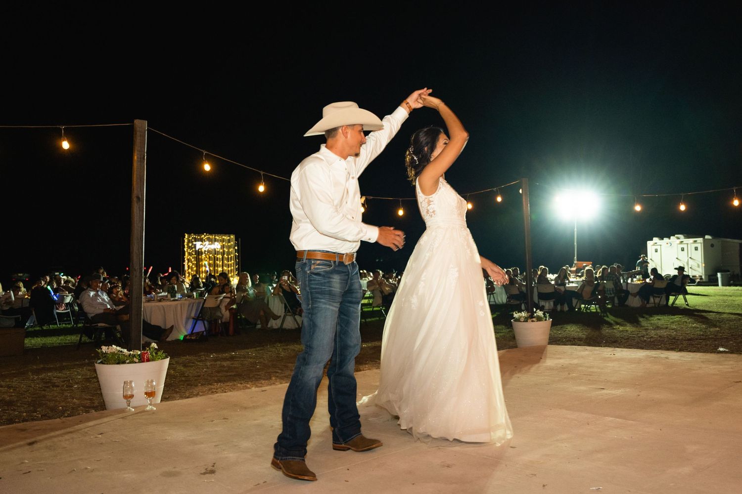 A couple dancing at an outdoor wedding reception with string lights overhead.