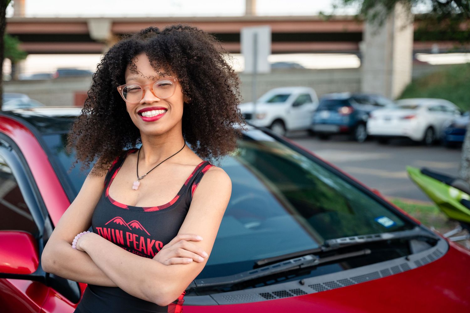 Person in casual attire standing beside red vehicle in parking lot.