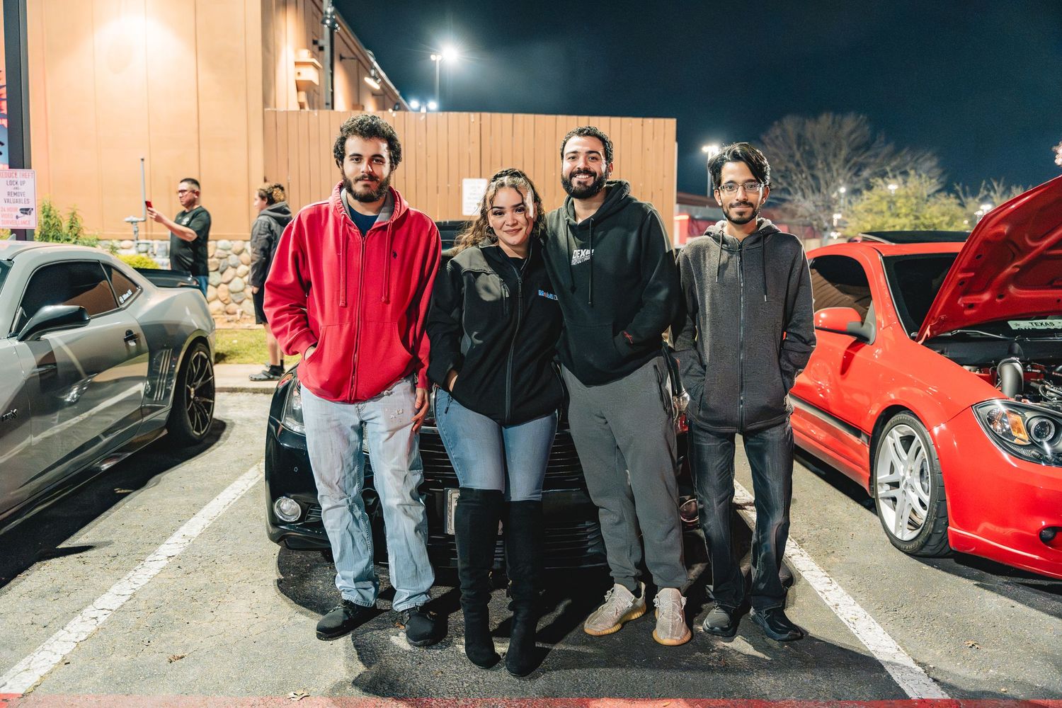 Group gathered at a casual nighttime car meet in a parking lot.