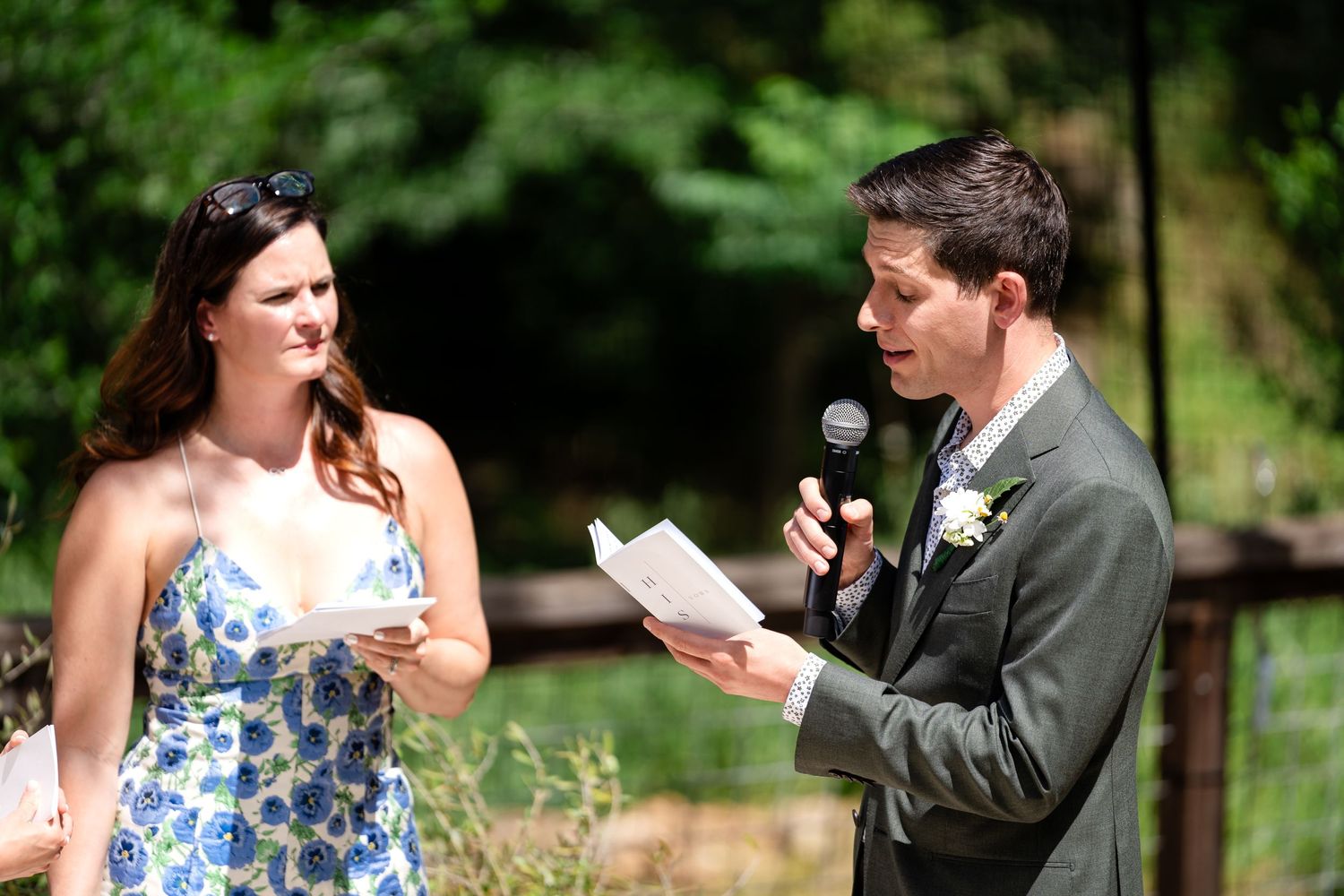 A wedding ceremony moment with readings being shared outdoors in a natural setting.