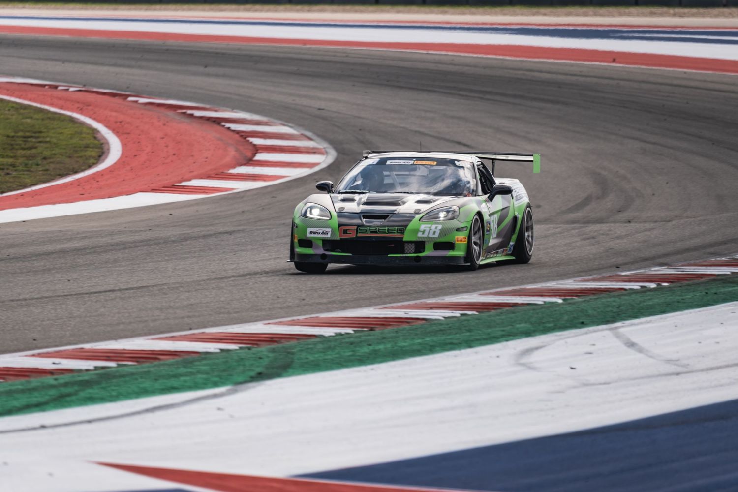 Green Porsche race car navigating a corner on a professional racing circuit.