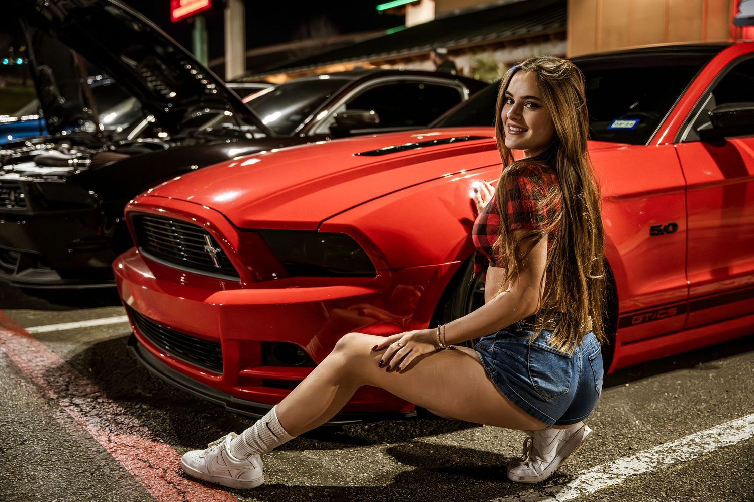 Car meet atmosphere with red sports car visible in dimly lit parking lot.