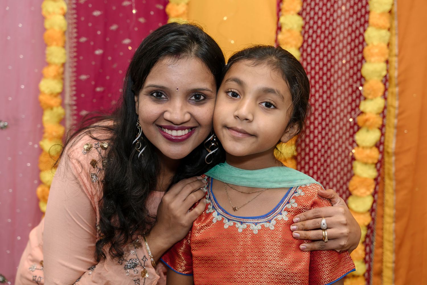 Mother and child in traditional Indian attire smiling against colorful decorative backdrop.