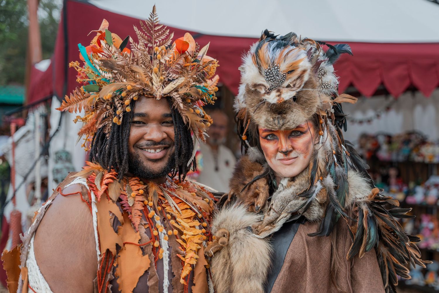 Two festival attendees wearing elaborate fantasy costumes with feathers and fur at renaissance faire.