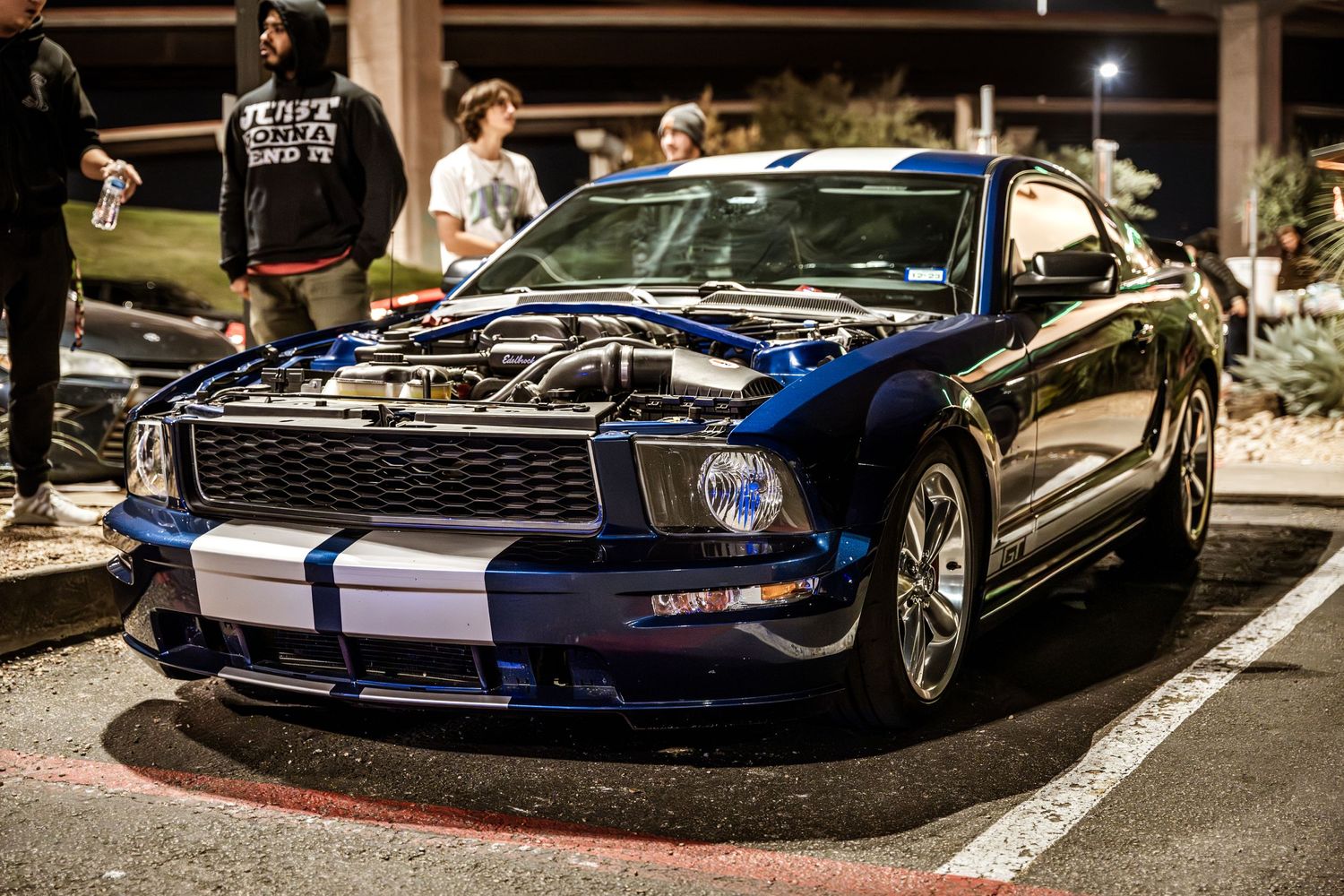 A black sports car with an open hood at a nighttime car show.