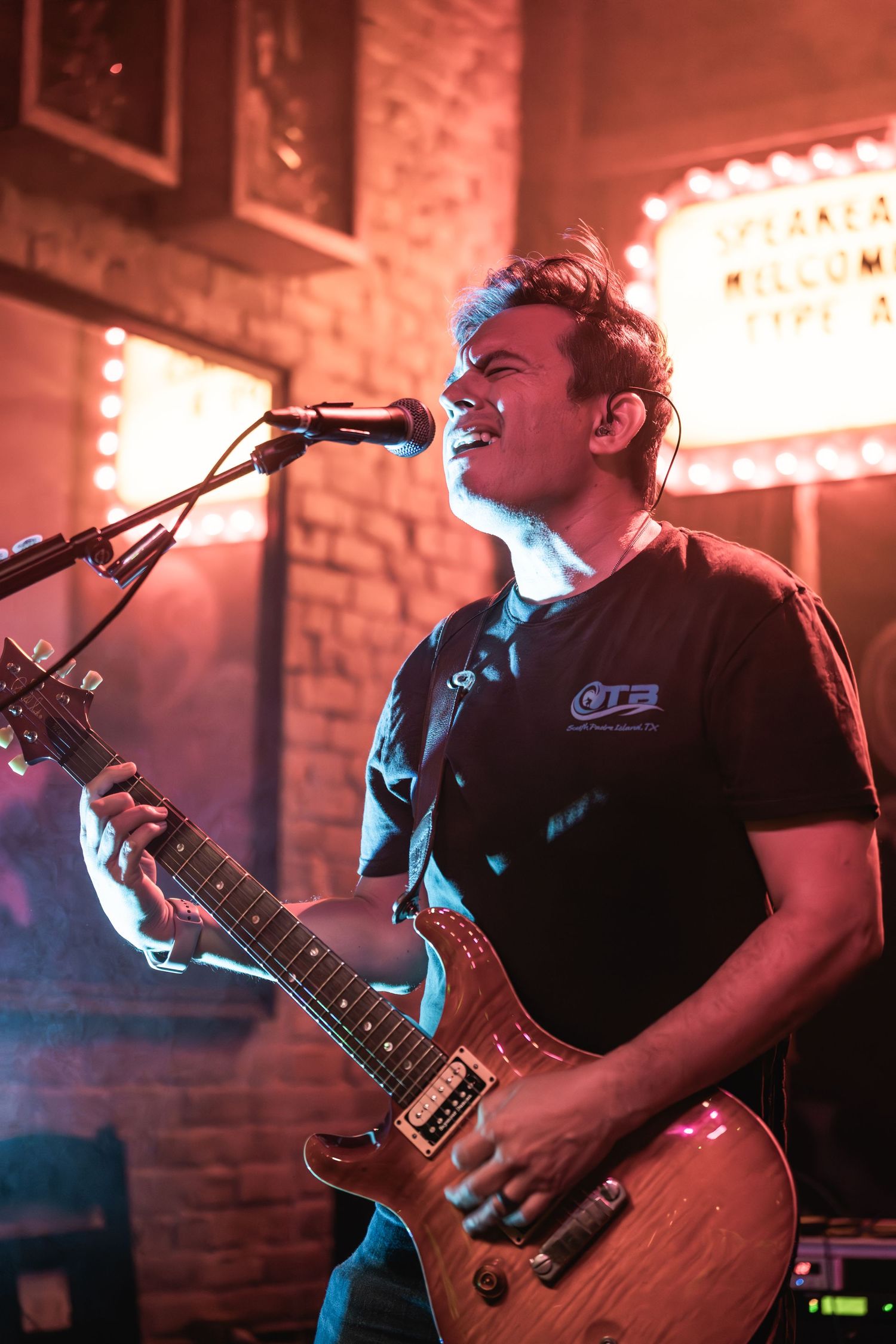 Guitarist performs passionately on stage under dramatic red lighting at an indoor venue.