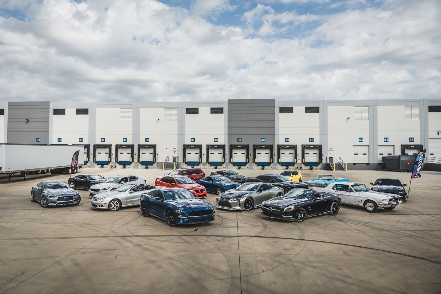 Luxury performance vehicles parked in front of a large warehouse loading dock with multiple bay doors.