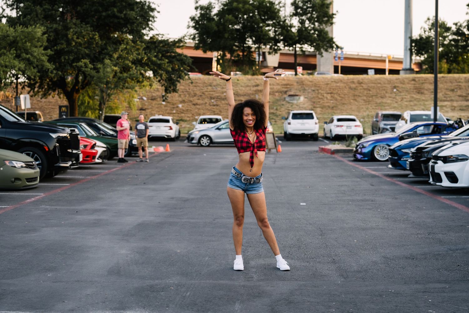 Person posing between parked cars in a parking lot.