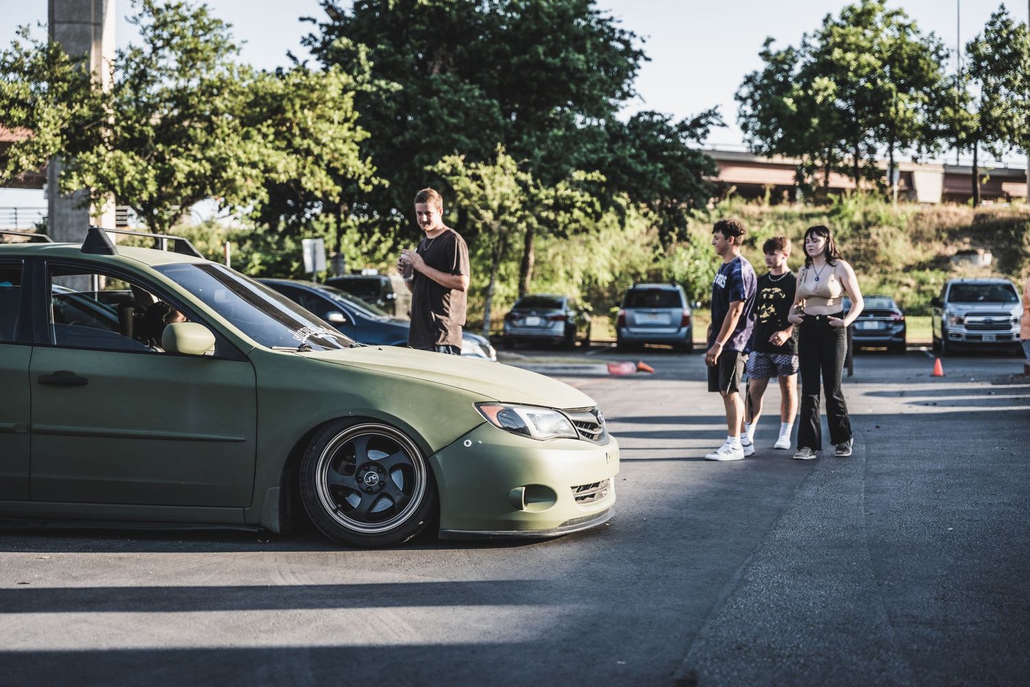 Custom lowered sedan at a car meet with spectators in the parking lot.