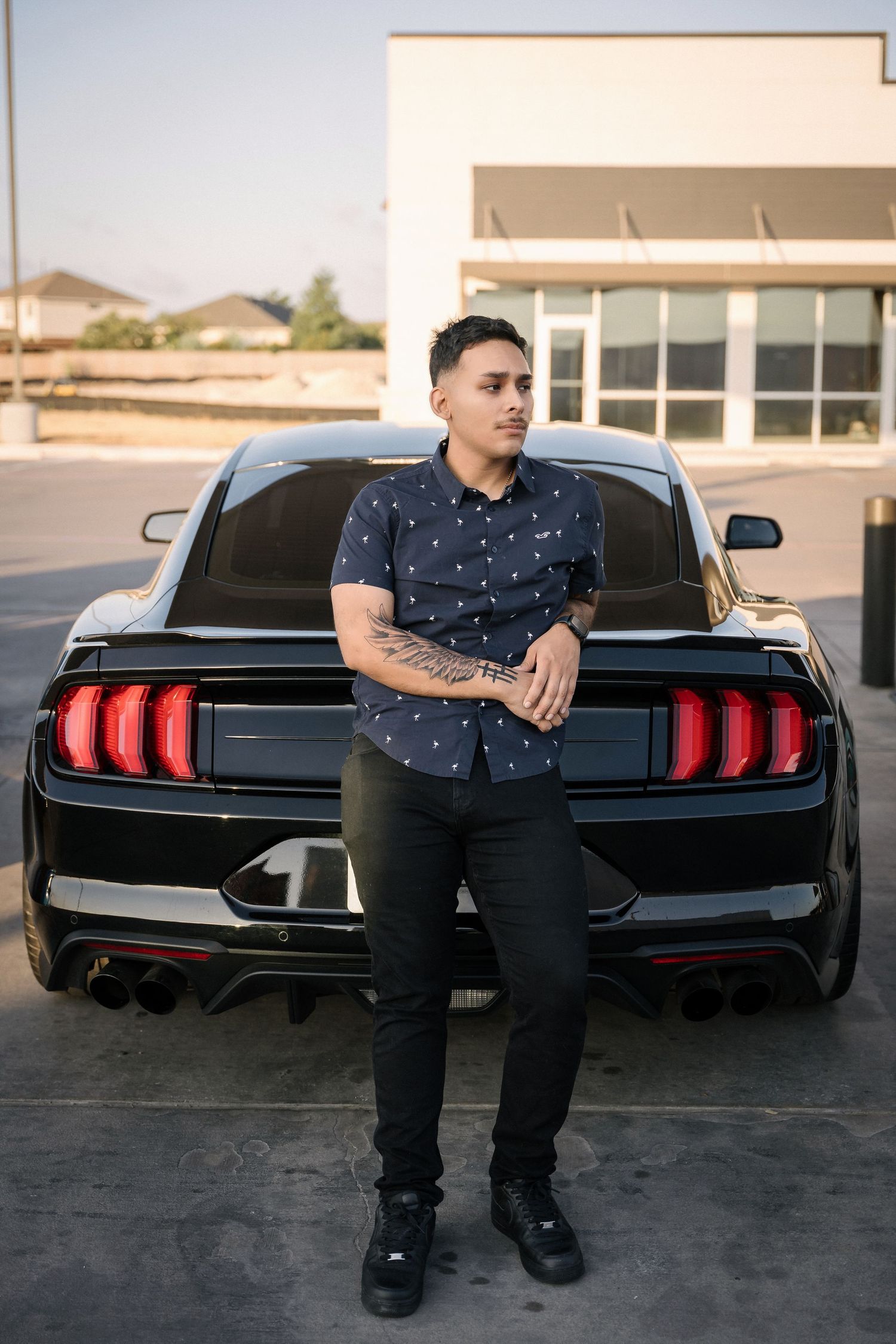 Person in polka dot shirt leaning against black Mustang with LED tail lights.