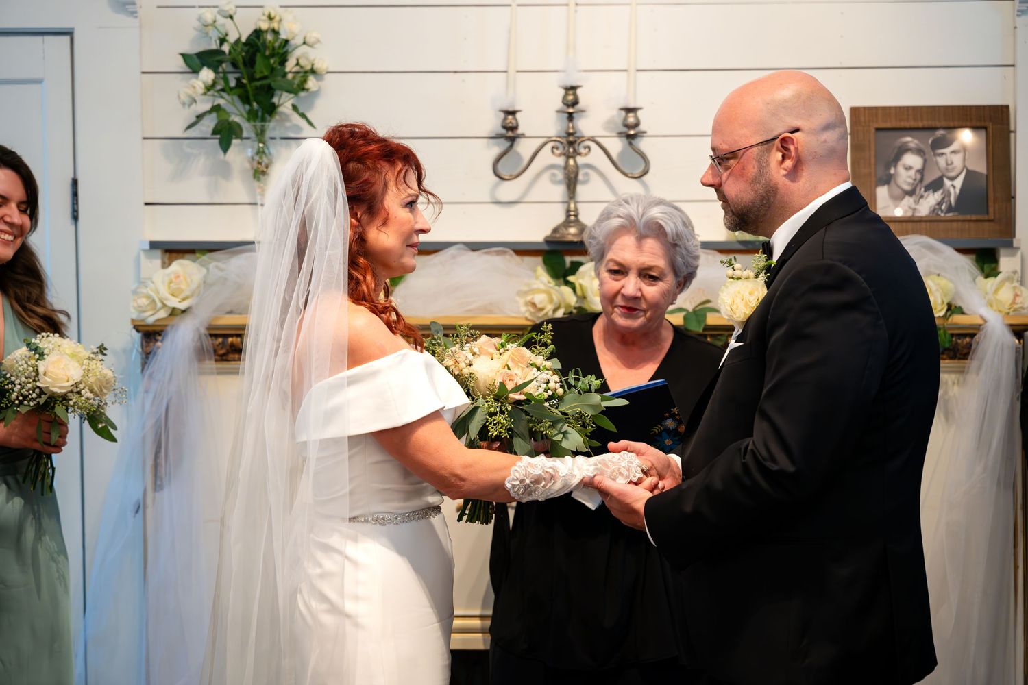 Wedding ceremony with couple exchanging vows in front of officiant with decorative chandelier.