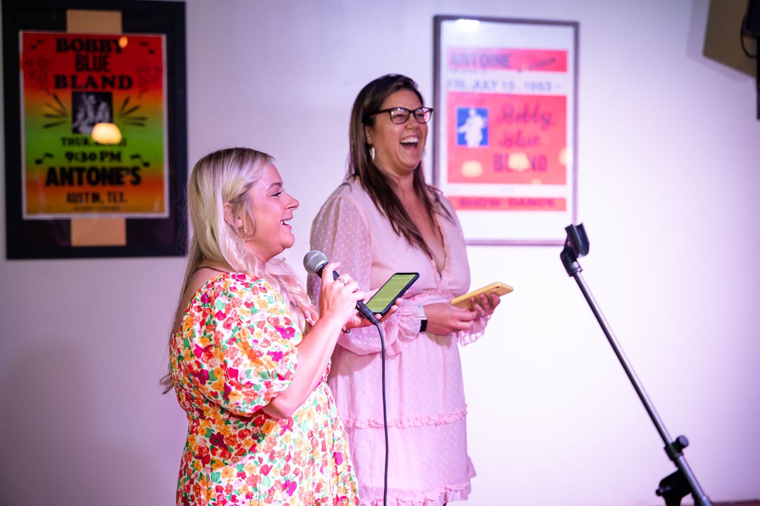 Two people laughing while performing karaoke in front of colorful wall art.