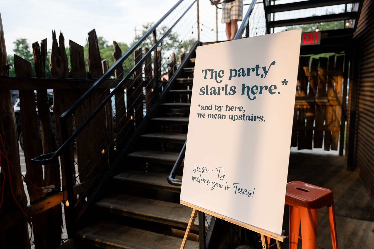Wedding directional sign with text 'The party starts here' on wooden stairs.