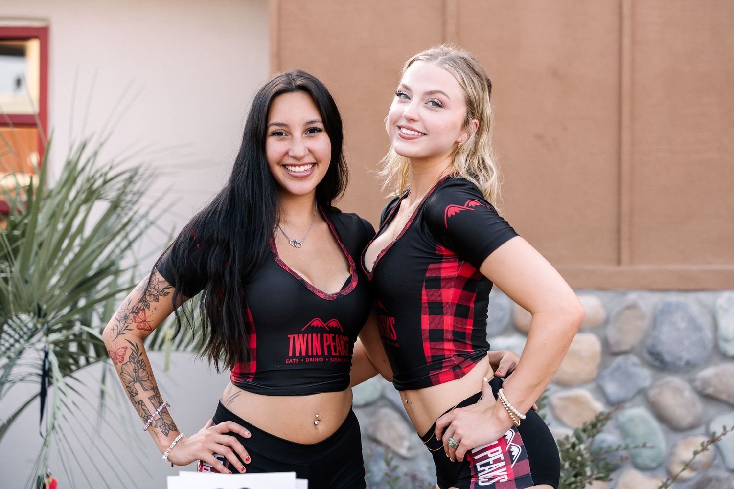 Two models in Twin Peaks branded attire posing against brown wall.