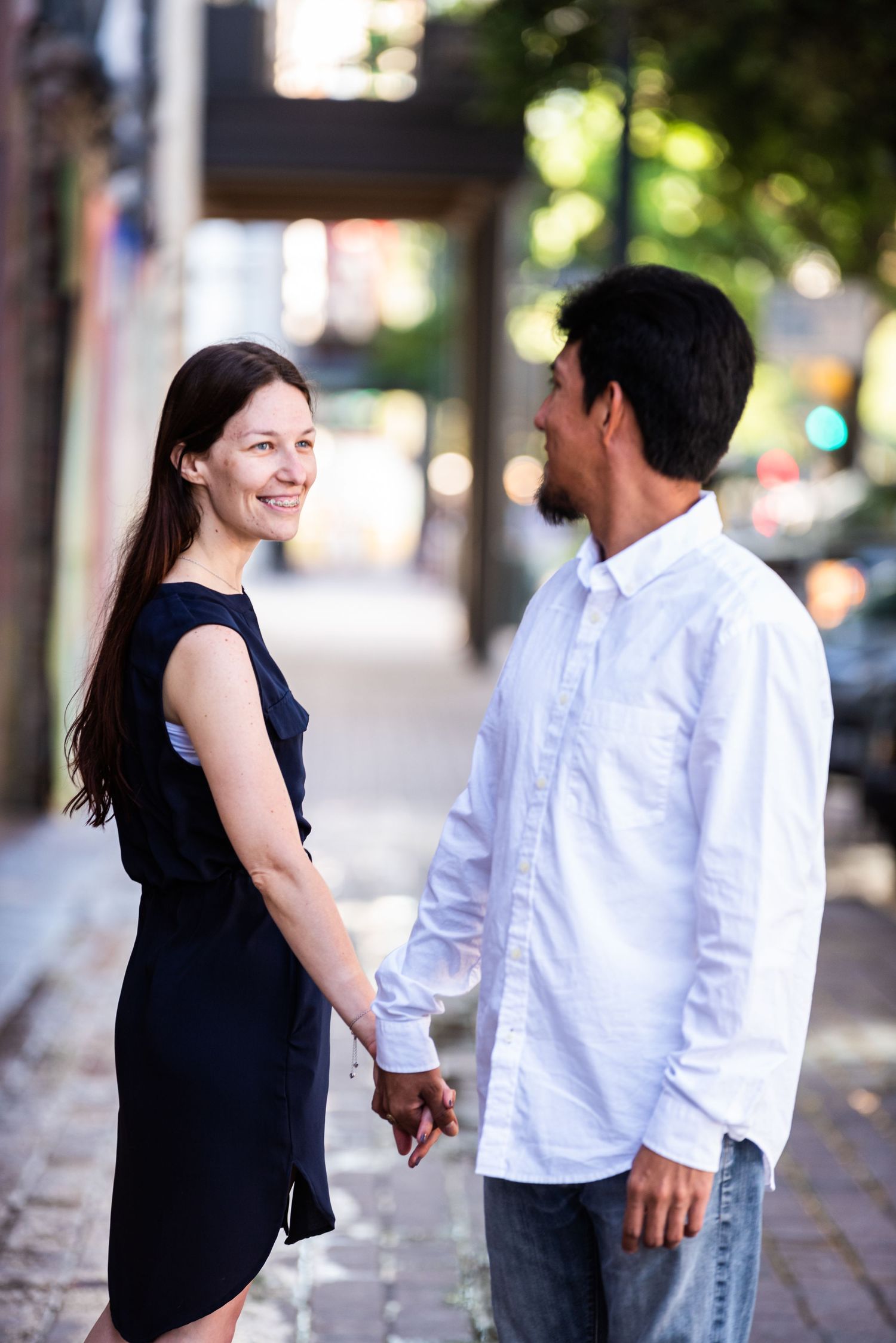 A candid engagement photo on a city sidewalk with natural lighting.