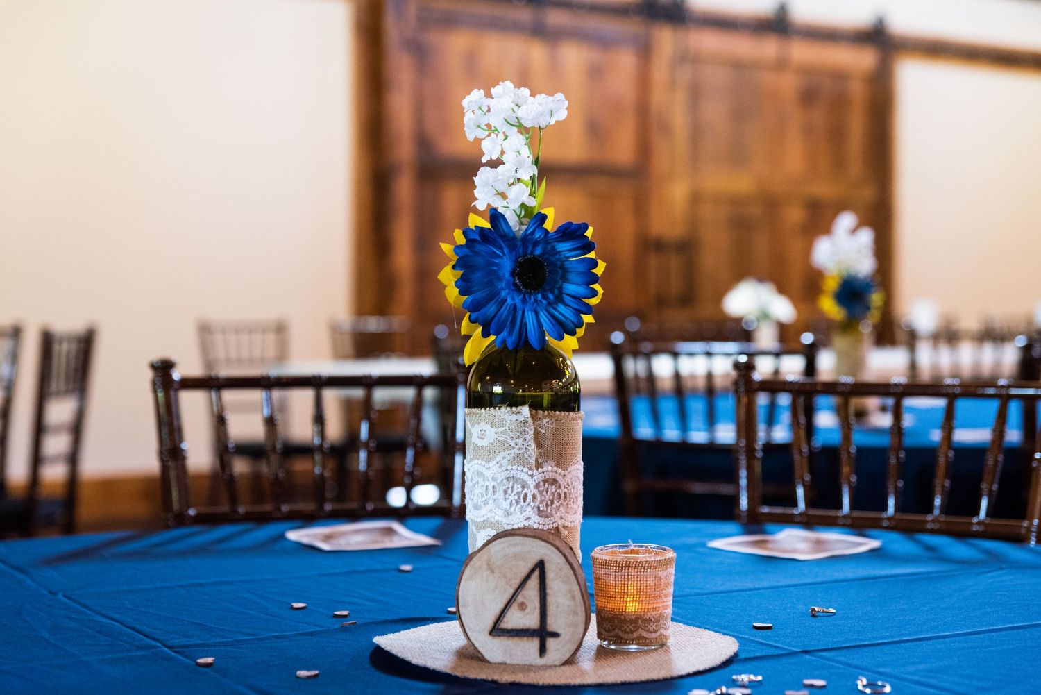 Wedding table centerpiece featuring blue sunflower and white flowers with table number 4.