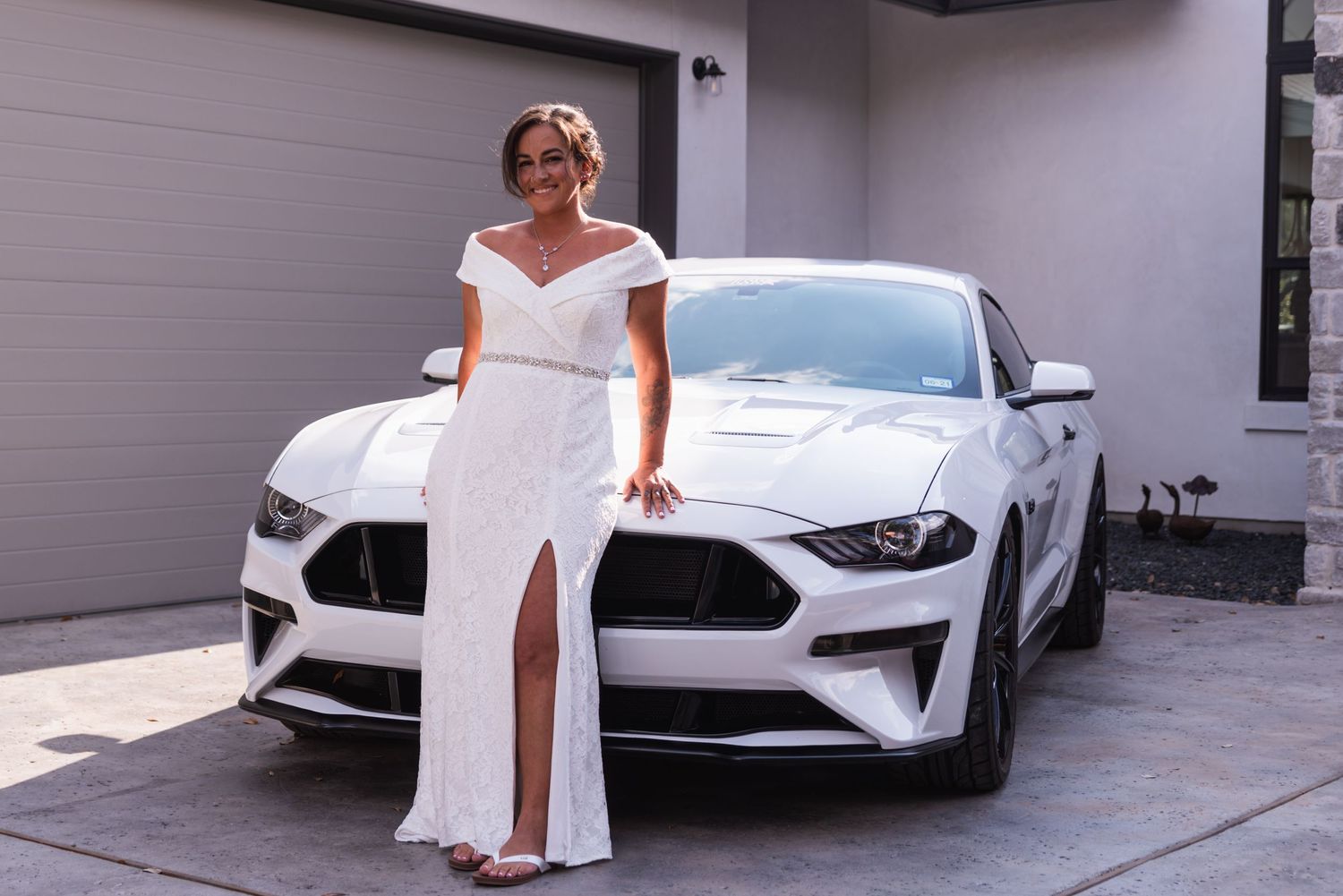Classic white bridal gown photographed with modern silver Mustang in driveway.