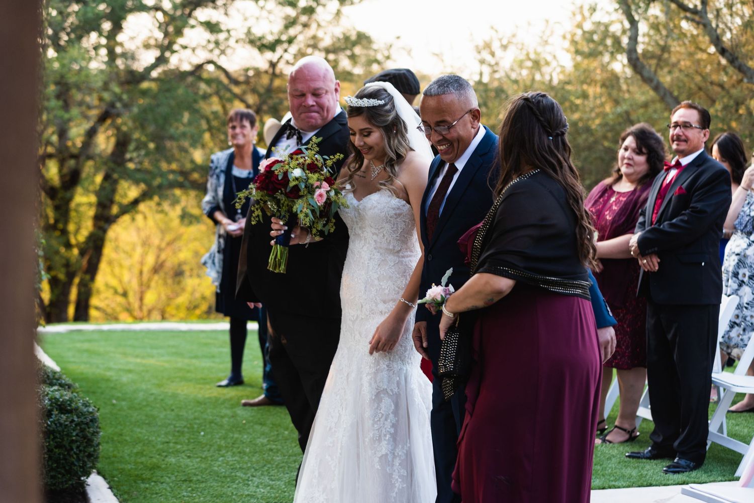 An outdoor wedding ceremony with attendees gathered on a lush green lawn at sunset.