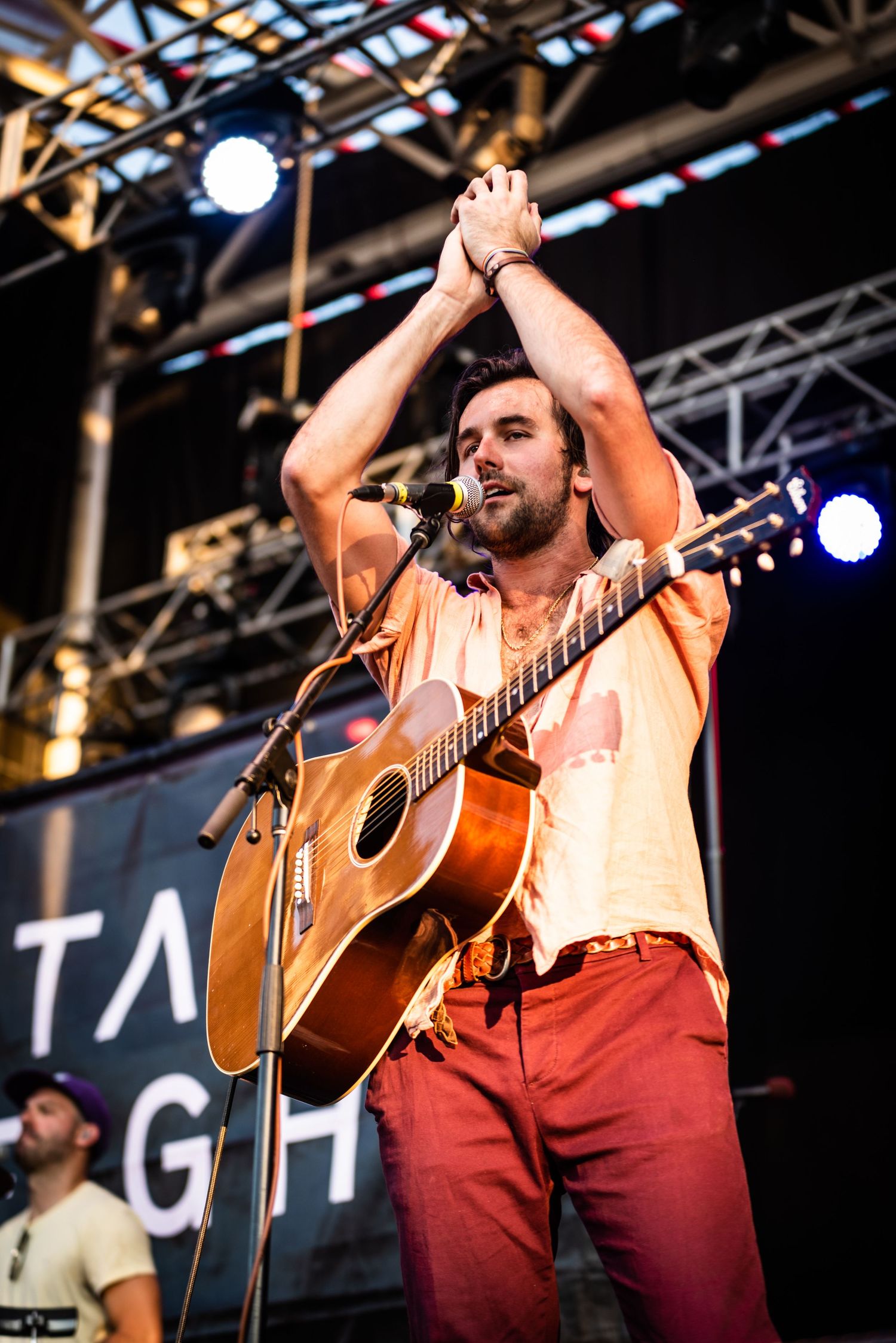 Performer raises hands during concert on stage with Tall Lights signage visible.