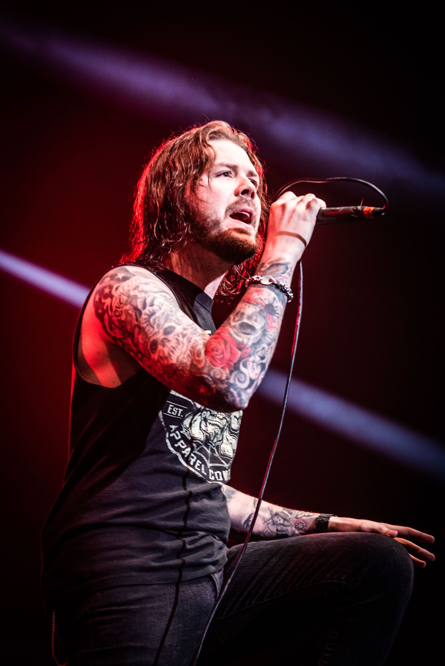 Tattooed vocalist performs on stage under dramatic red and purple lighting effects.