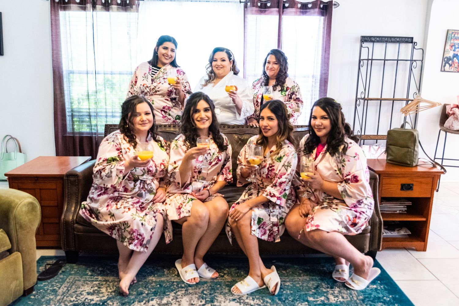 Wedding party in floral robes poses together on couch during pre-ceremony preparations.