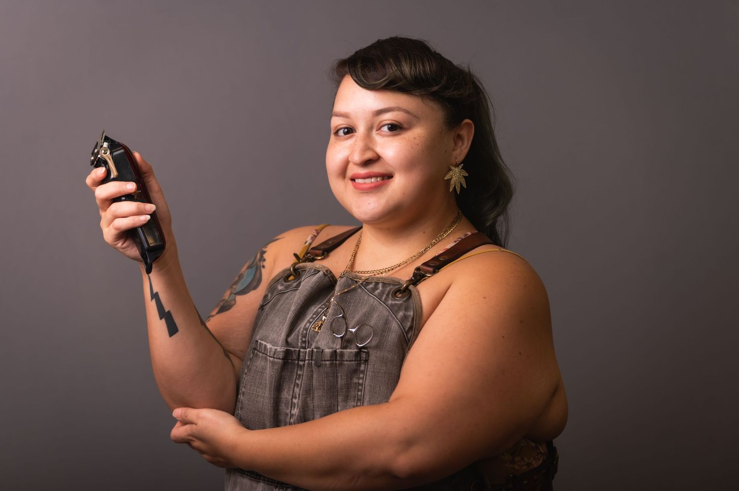 Stylist in denim overalls holding grooming tools in studio setting.