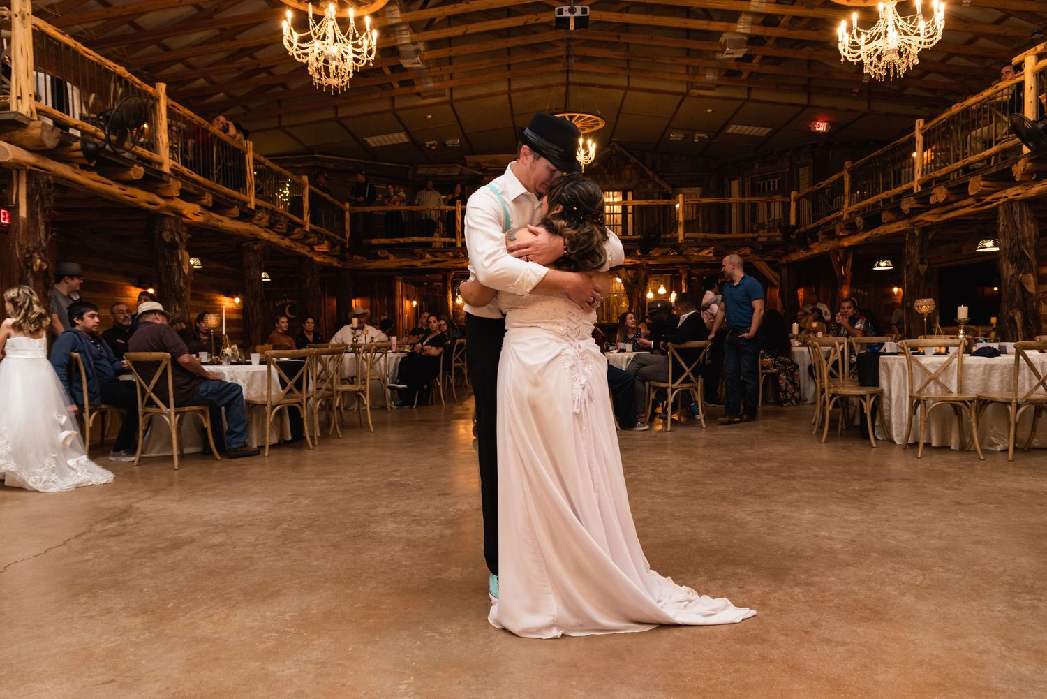 A couple shares their first dance in a rustic barn venue with chandeliers overhead.