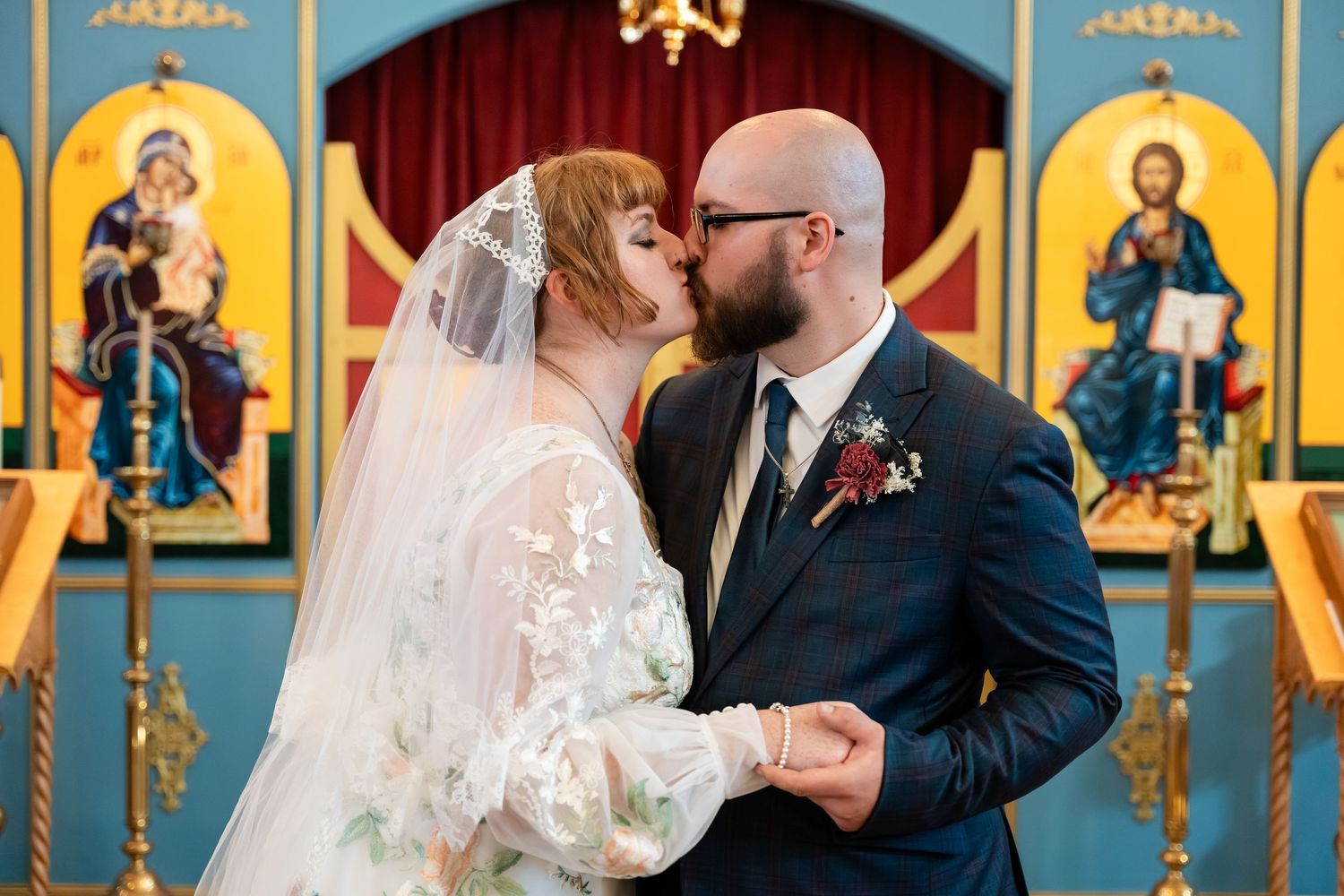 Two people share a tender moment during an Orthodox church wedding ceremony with ornate icons in the background.
