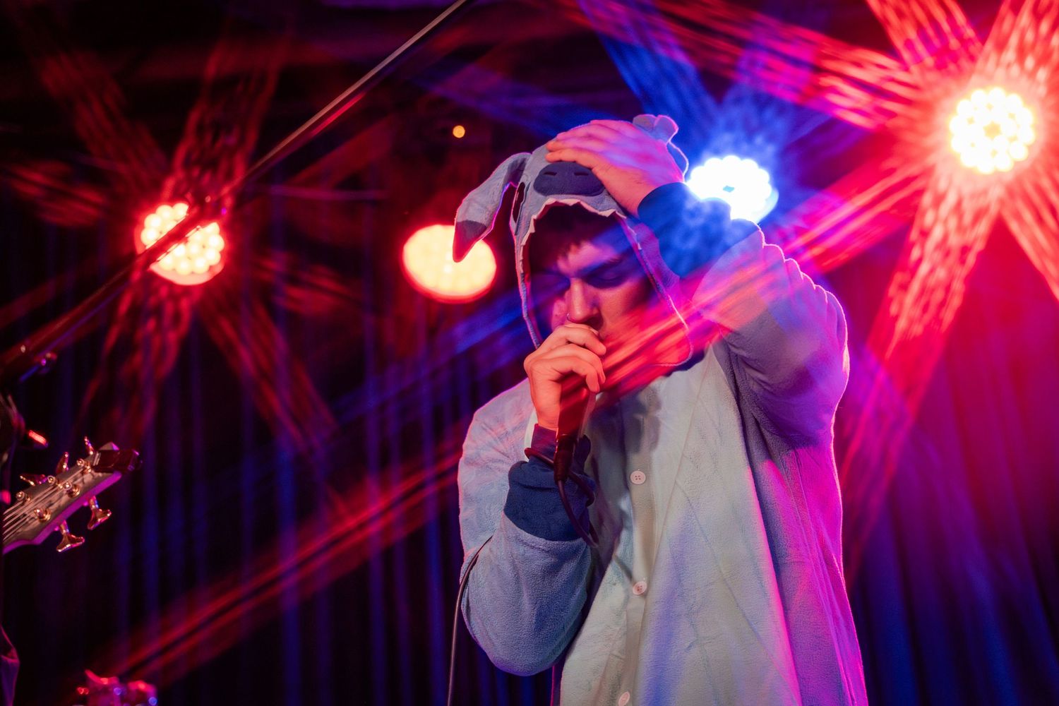 A performer singing on stage with dramatic red and blue lighting effects creating a dynamic concert atmosphere.