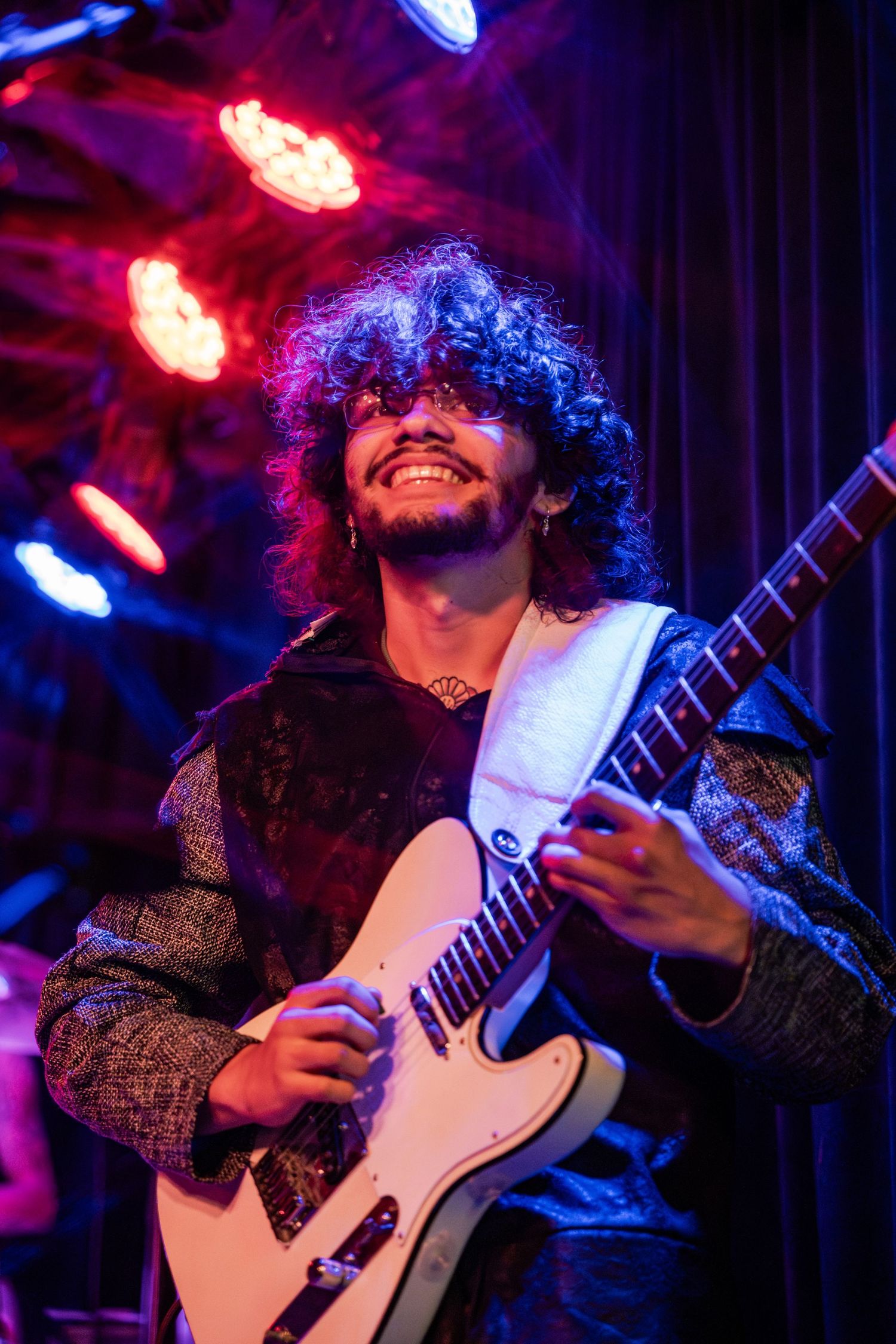 Musician performs passionately on stage with white guitar under dramatic blue and red stage lighting.