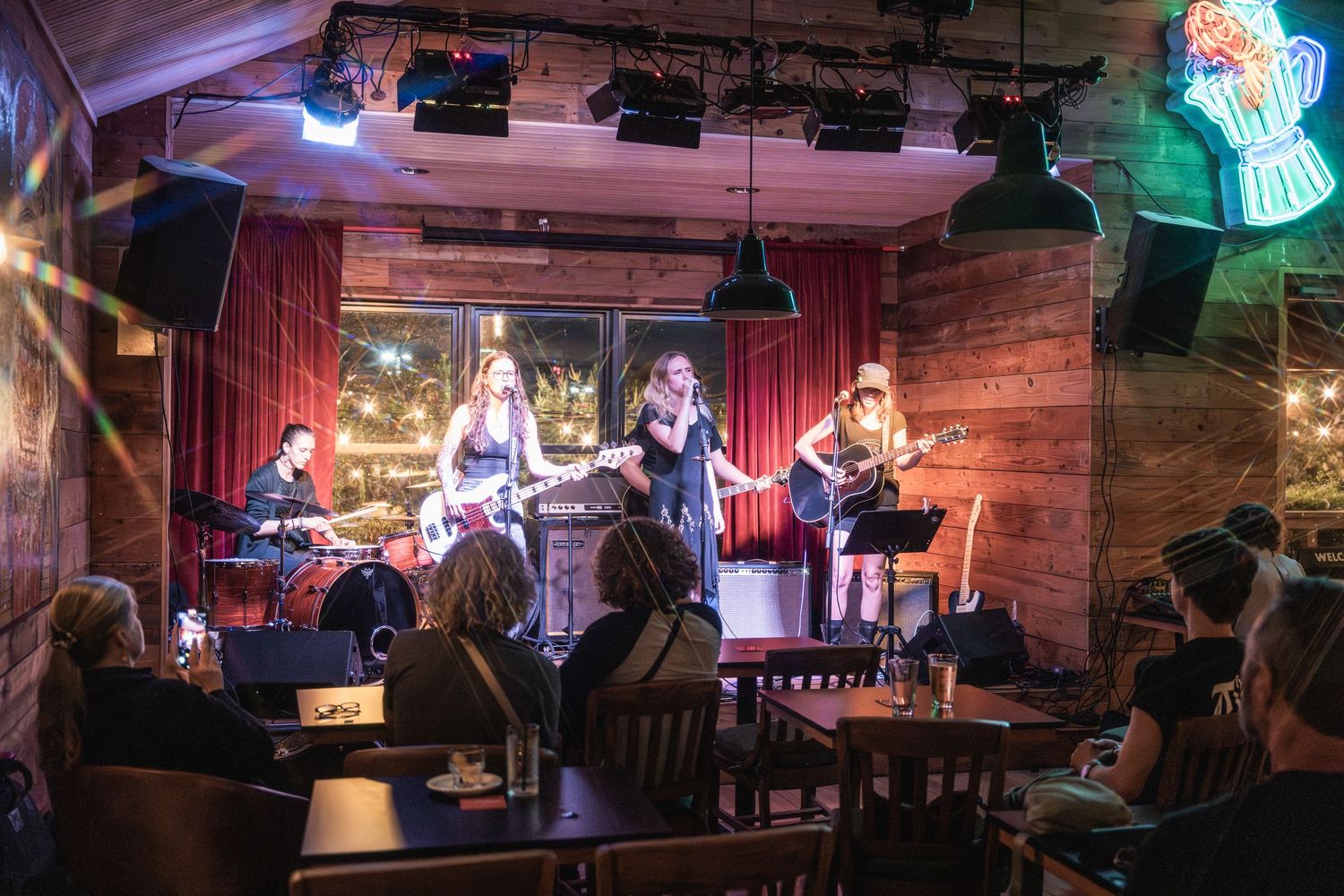 Musicians perform on stage in a dimly lit brick-walled venue with red curtains and atmospheric lighting.